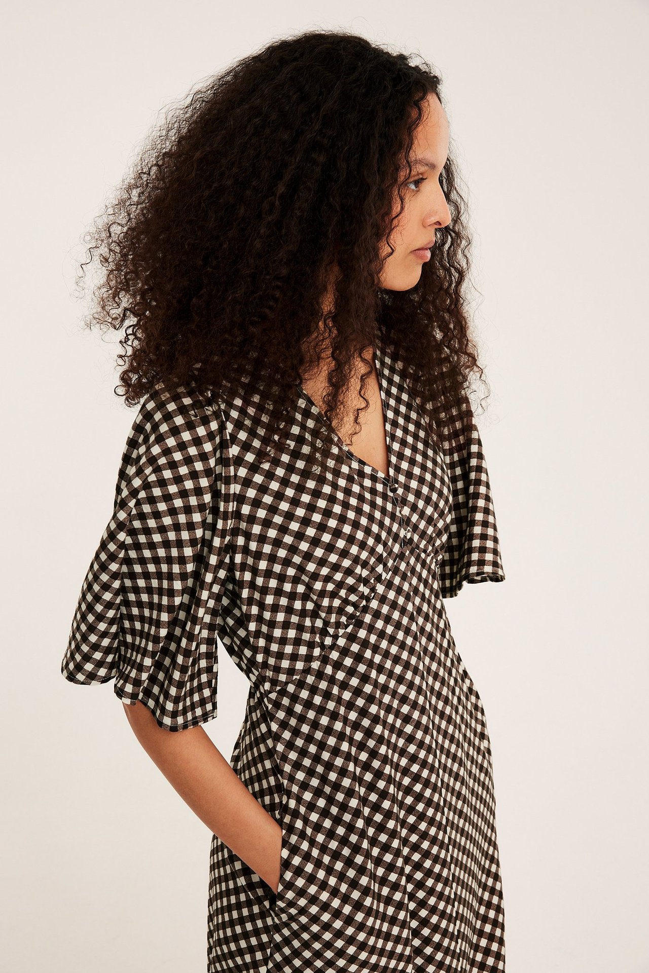 Sidovy av en kvinna i brun- och vitrutig midiklänning med knappar fram och volangärmar.