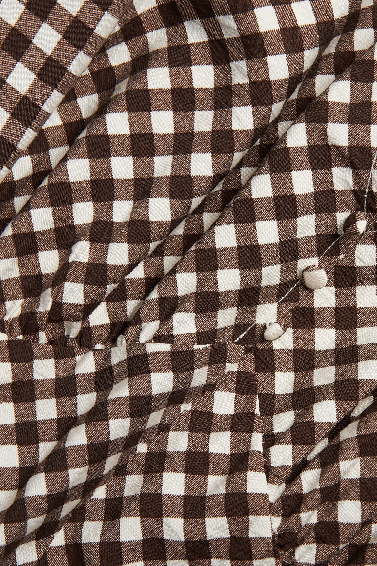 Lähikuva ruskeavalkoisesta ruudullisesta mekkokankaasta ja pienistä napeista.