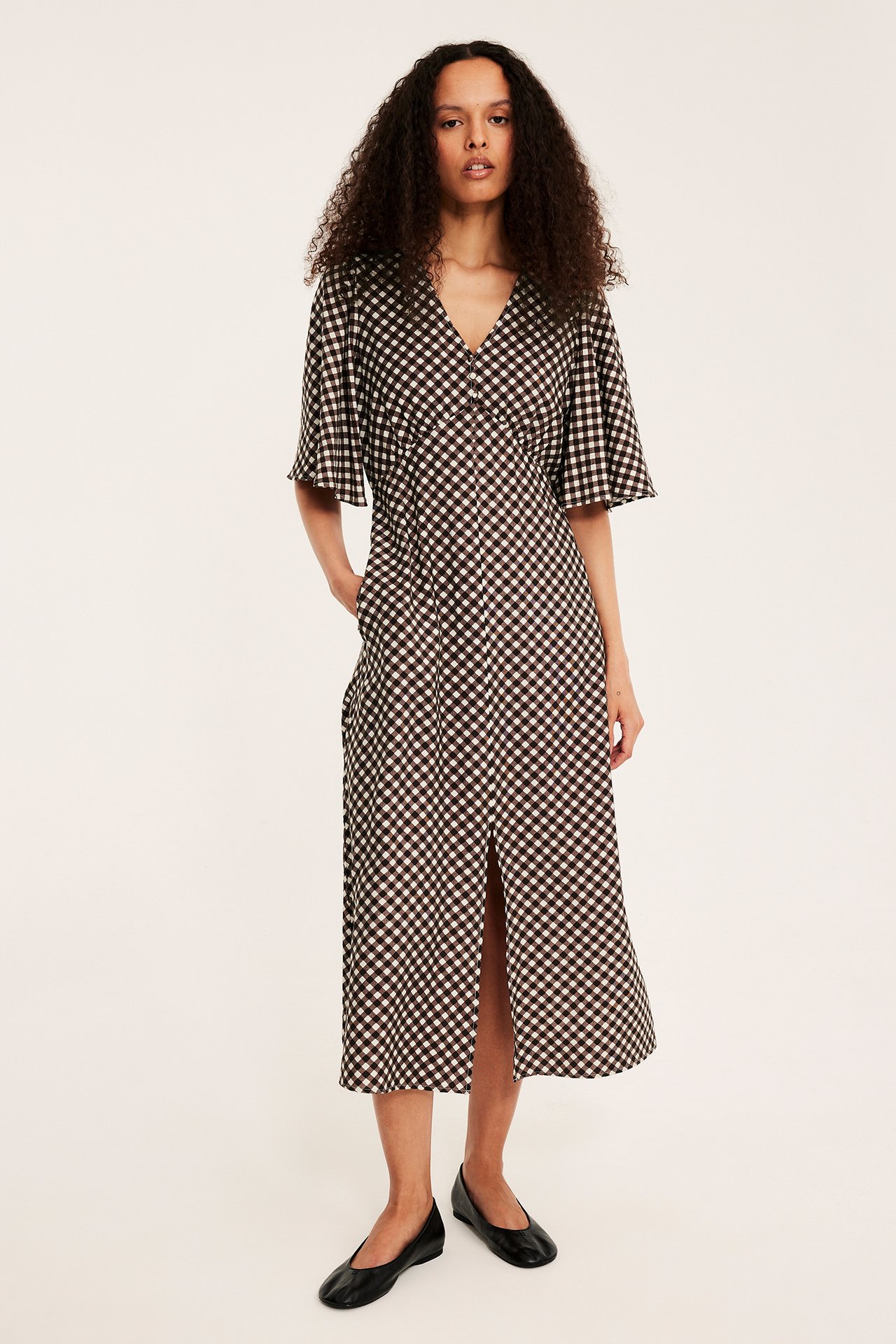 Framsida: kvinna i brunvit mönstrad midiklänning med knappar, volangärmar och svarta platta skor.