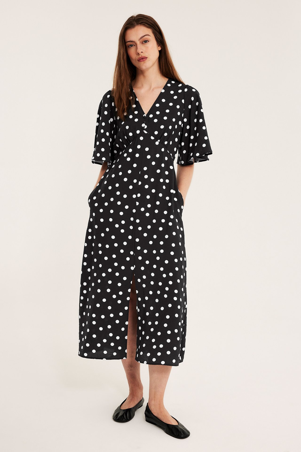 En kvinna bär en svartprickig midiklänning med volangärmar och knappar fram, samt svarta ballerinaskor.