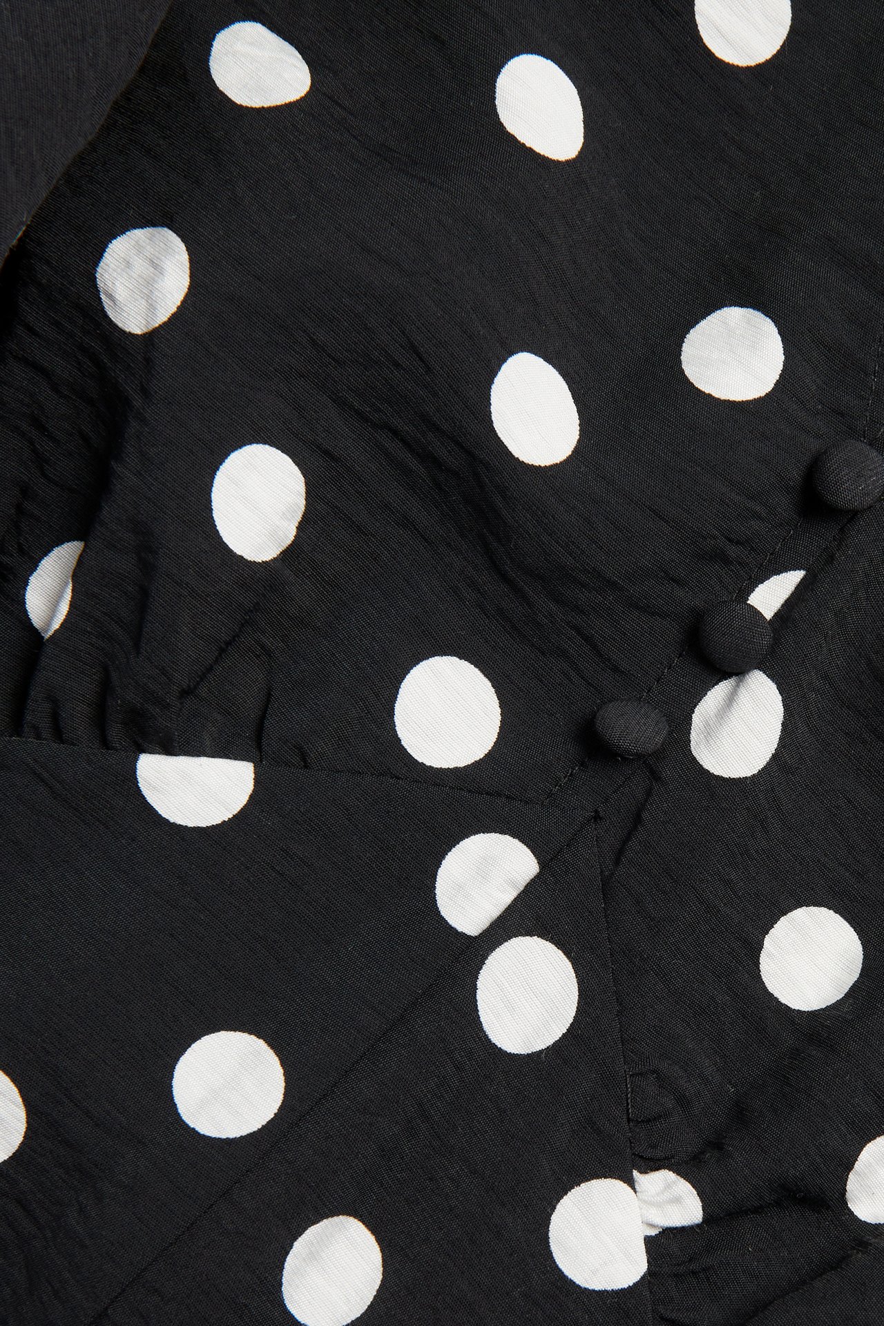 Närbild på en svart mönstrad klänning med vita prickar och svarta knappar framtill.