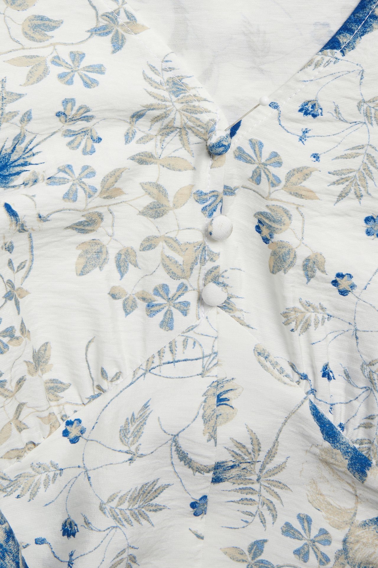 Zbliżenie białej wiskozowej sukienki z niebiesko-beżowym wzorem kwiatowym, trzy białe guziki.