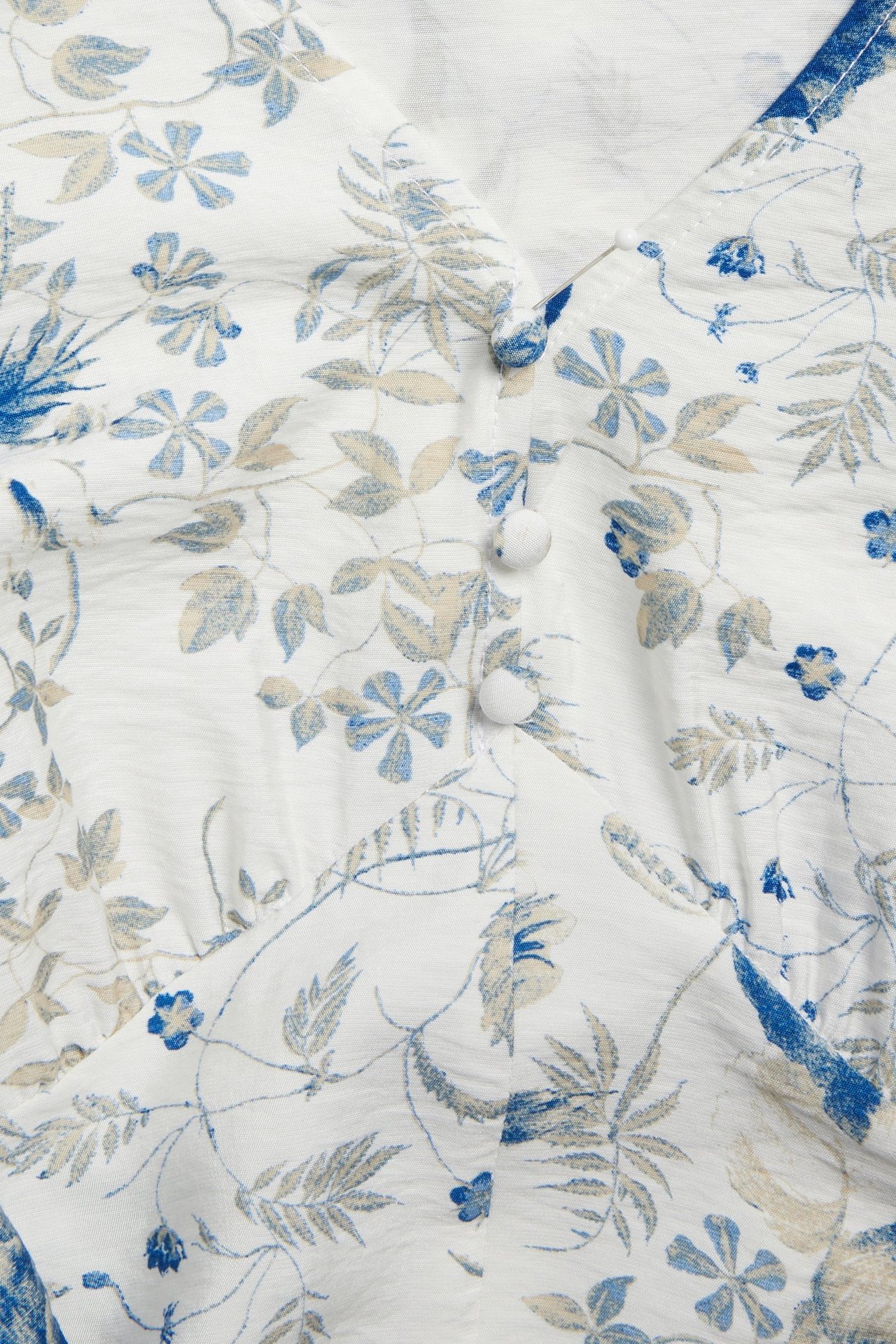 Zbliżenie białej wiskozowej sukienki z niebiesko-beżowym wzorem kwiatowym, trzy białe guziki.