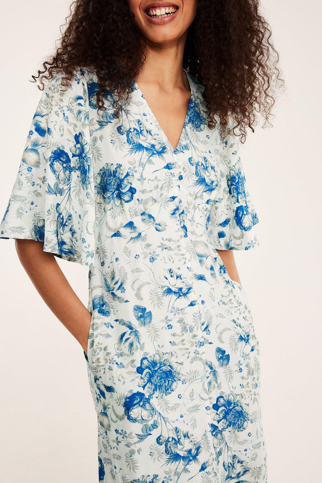 Etunäkymä: Nainen yllään vaaleansininen kukkakuvioinen midimekko V-pääntiellä, napeilla ja frillahihoilla.