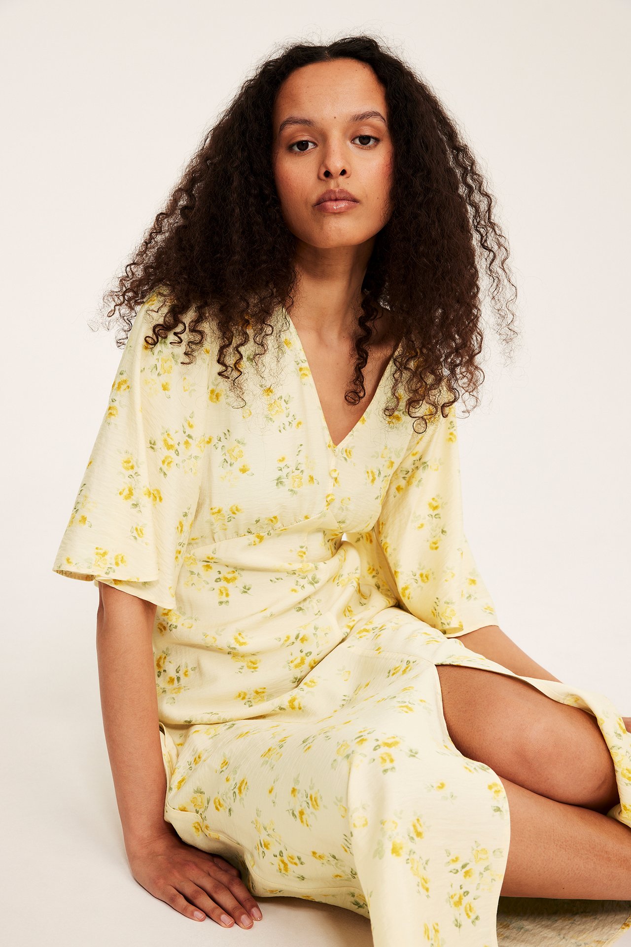 Framifrån, kvinna i ljusgul blommig midiklänning med knappar framtill och volangärmar.