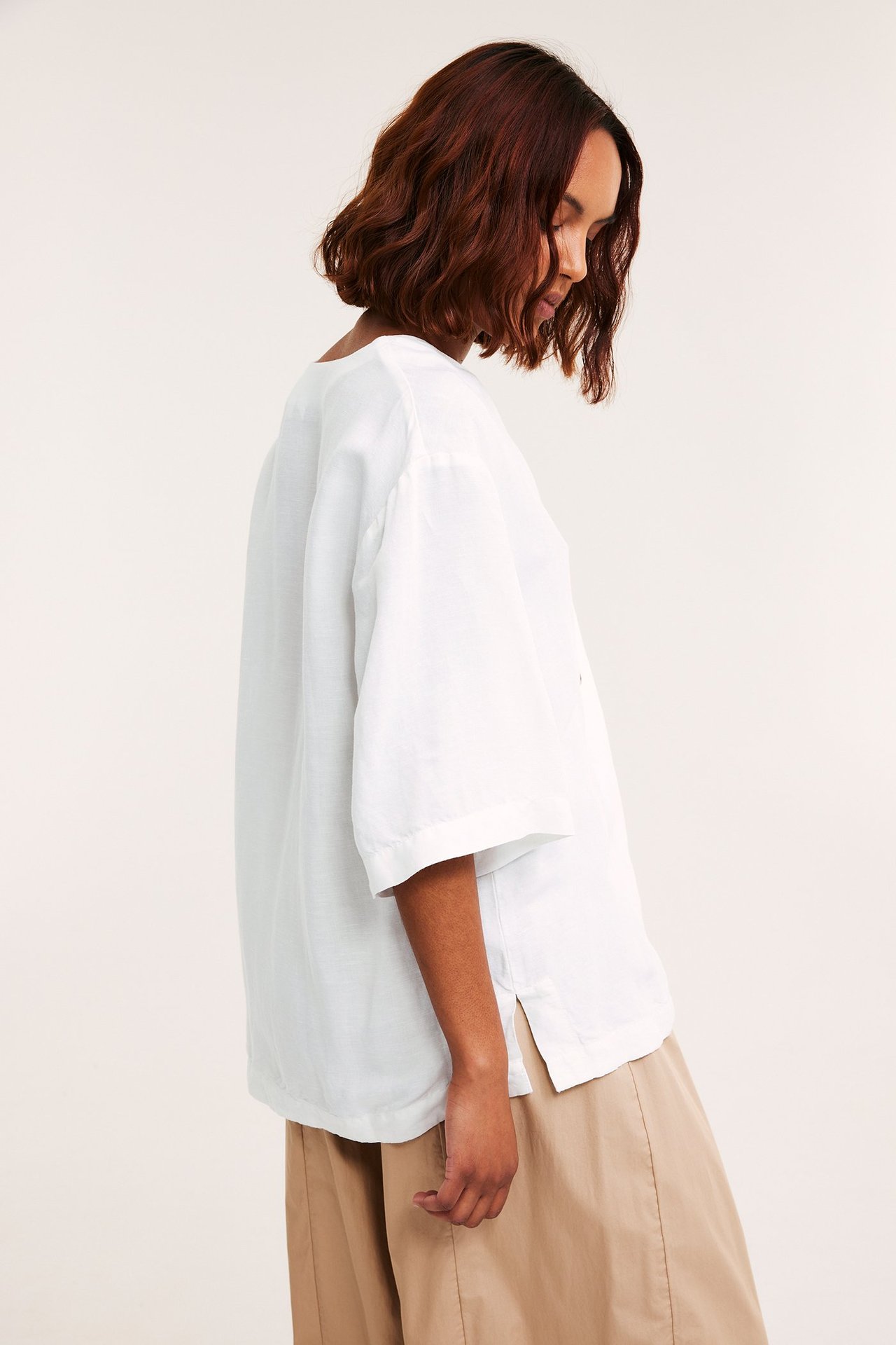 Sidovy av en kvinna i en lös vit kortärmad linneblandningsskjorta med ljusbruna vida byxor.