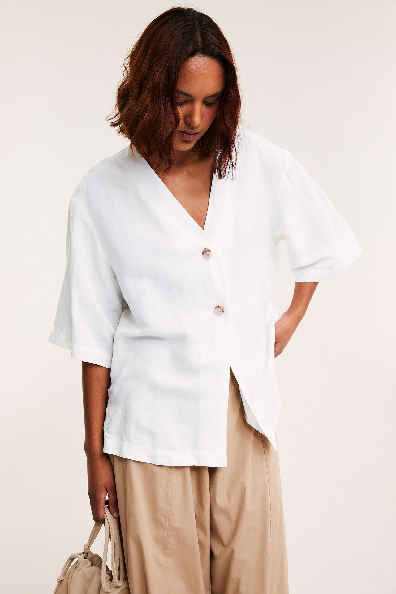 Framifrån: Kvinna i vit kortärmad skjorta i linnemix med två knappar och ljusbruna byxor.