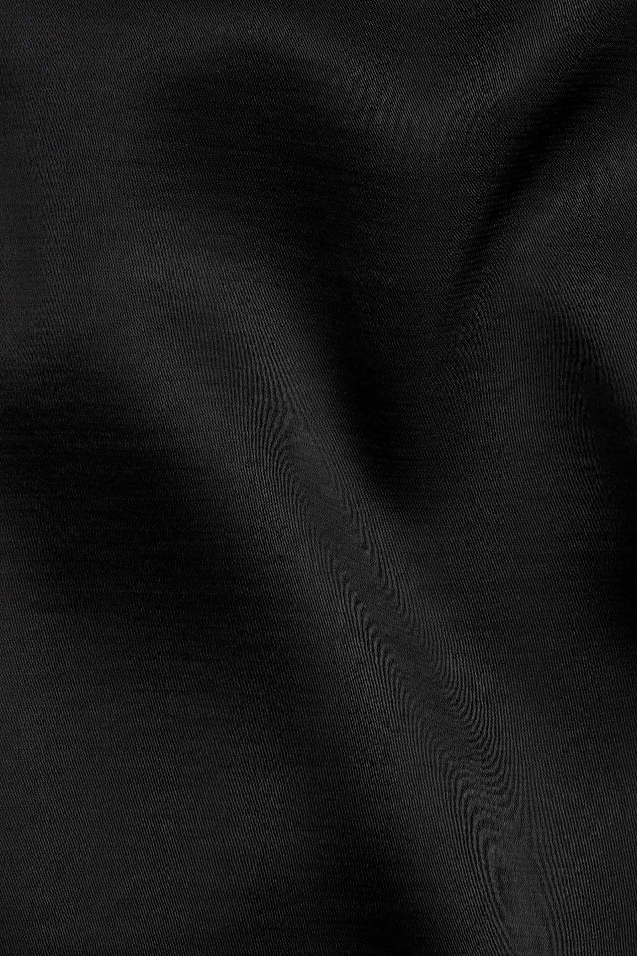 Lähikuva mustasta, yksivärisestä satiinikankaan pinnasta, jossa on hienovarainen kiilto ja poimuja.