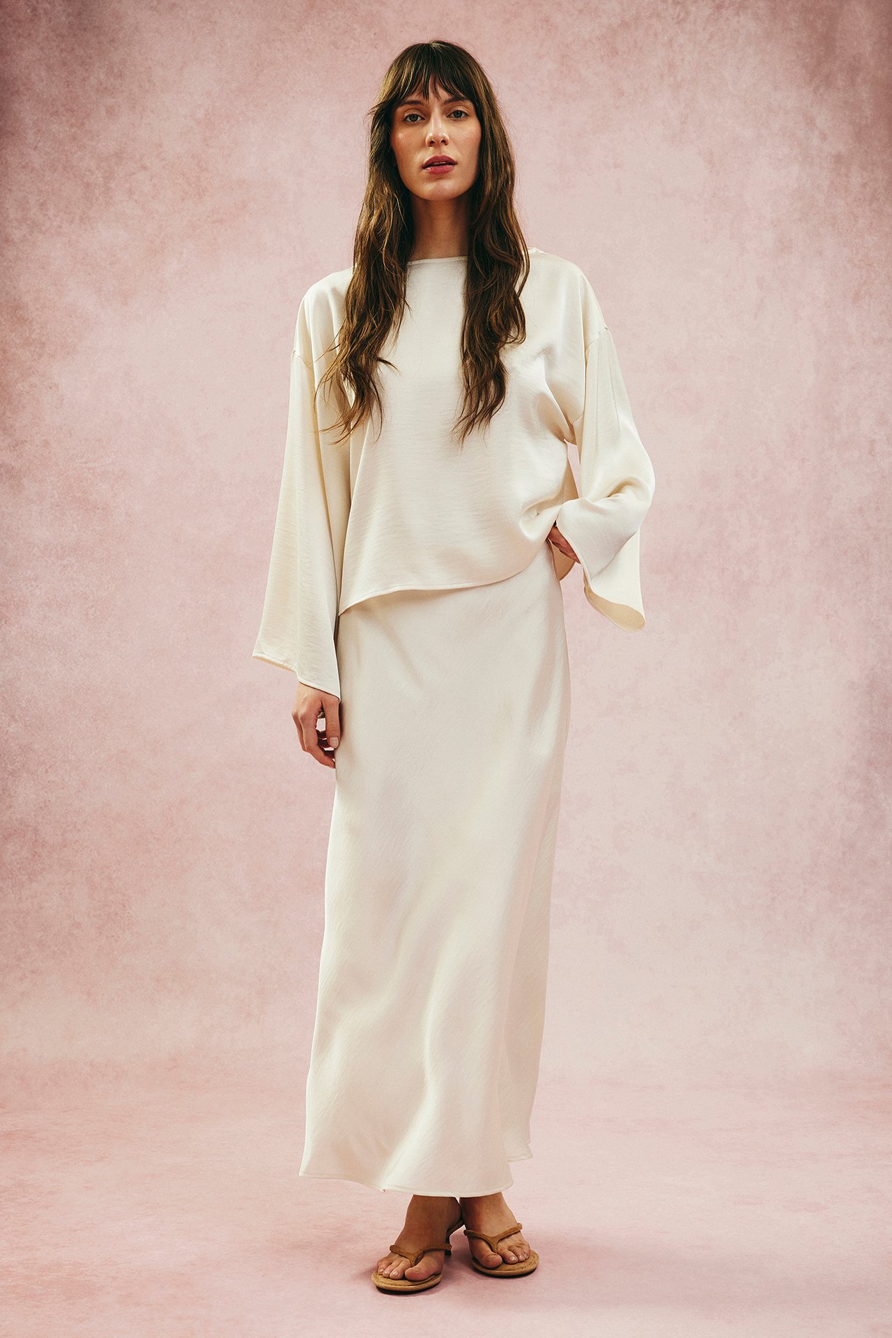 Edestäpäin: Nainen yllään offwhite leveähihainen satiinipusero, yhteensopiva pitkä hame ja ruskeat sandaalit.