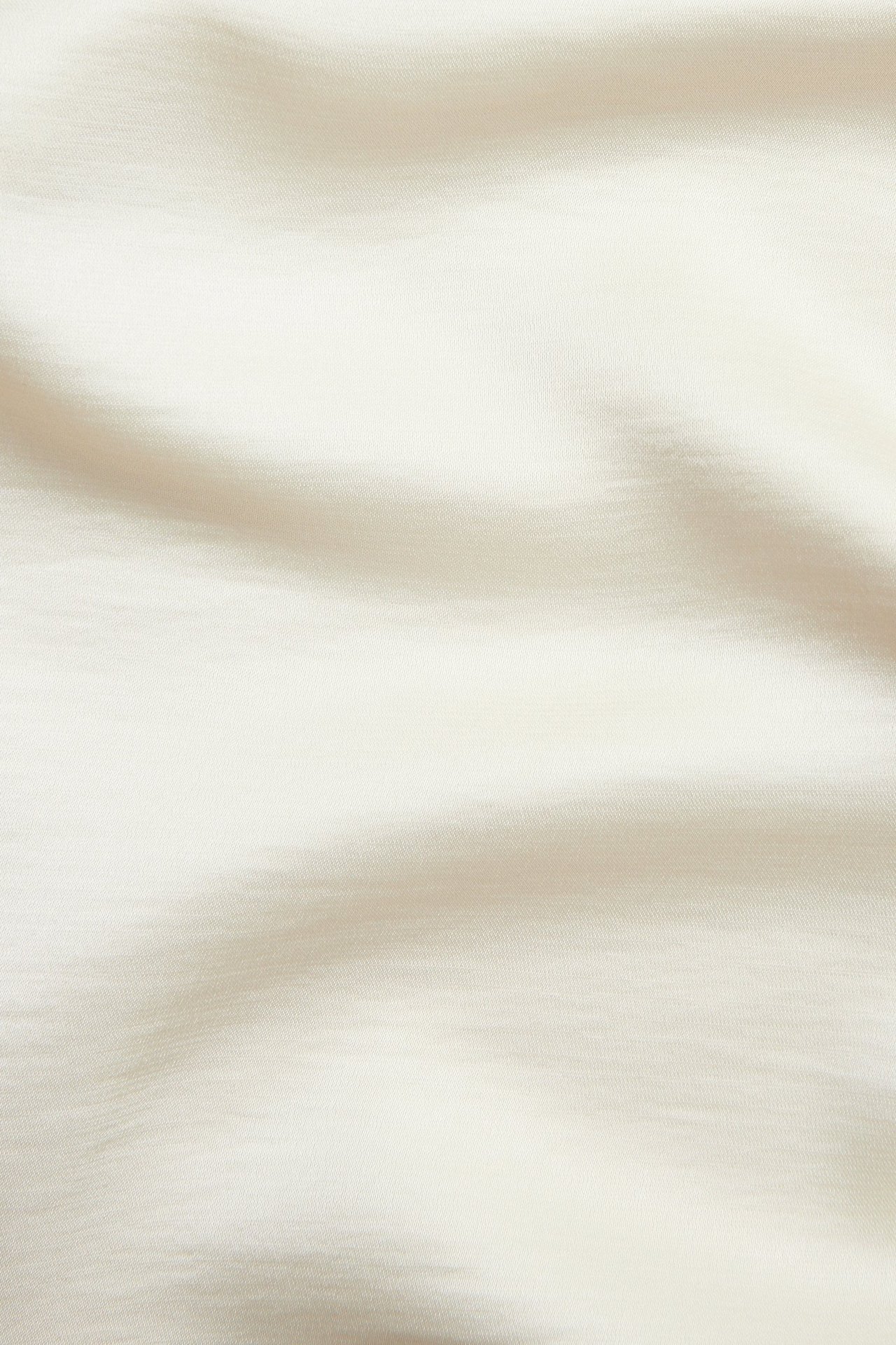 Zbliżenie na kremowy, jednolity satynowy materiał z miękkimi fałdami.