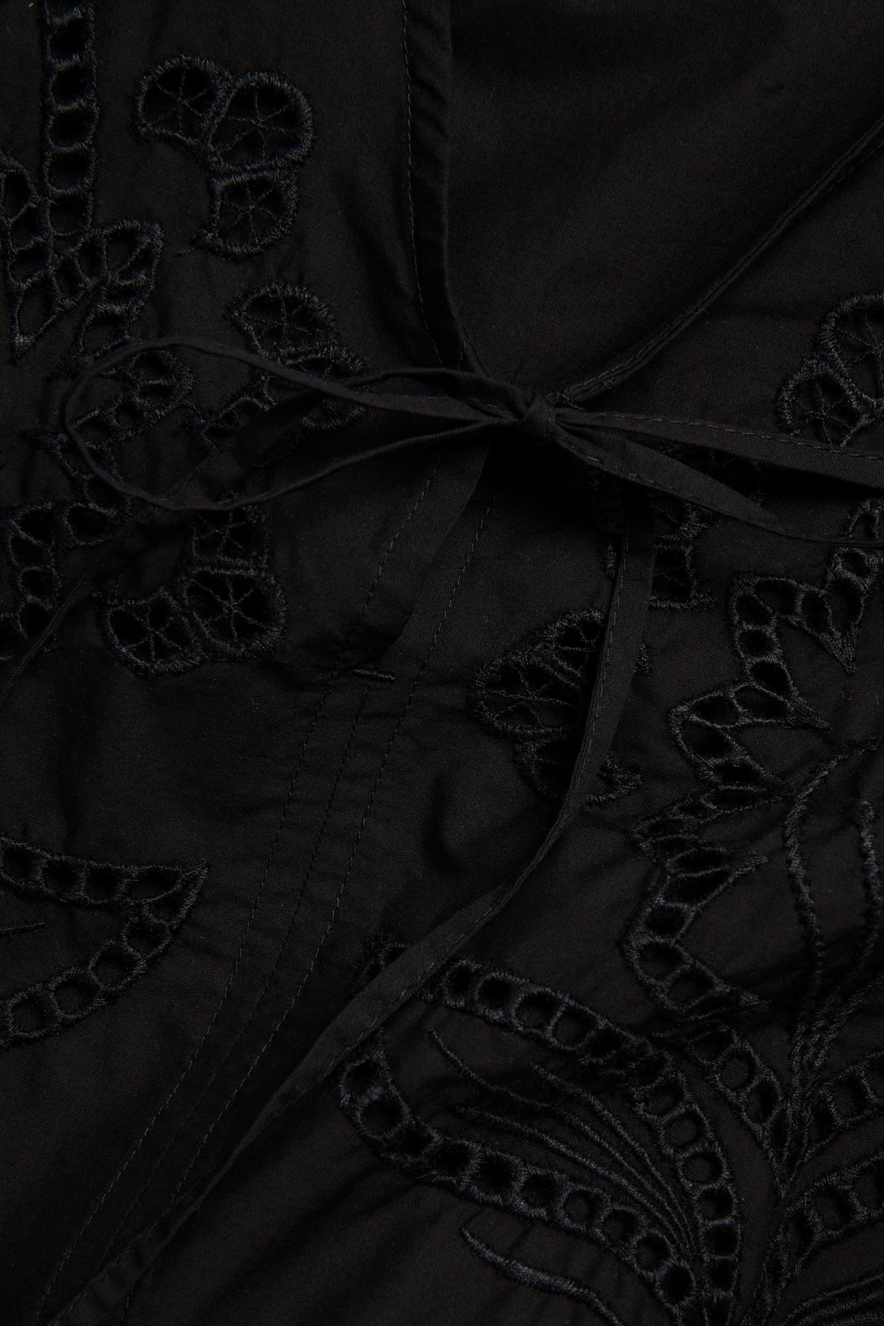Zbliżenie czarnej bluzki z popeliny bawełnianej z haftem i wiązaniem w talii.