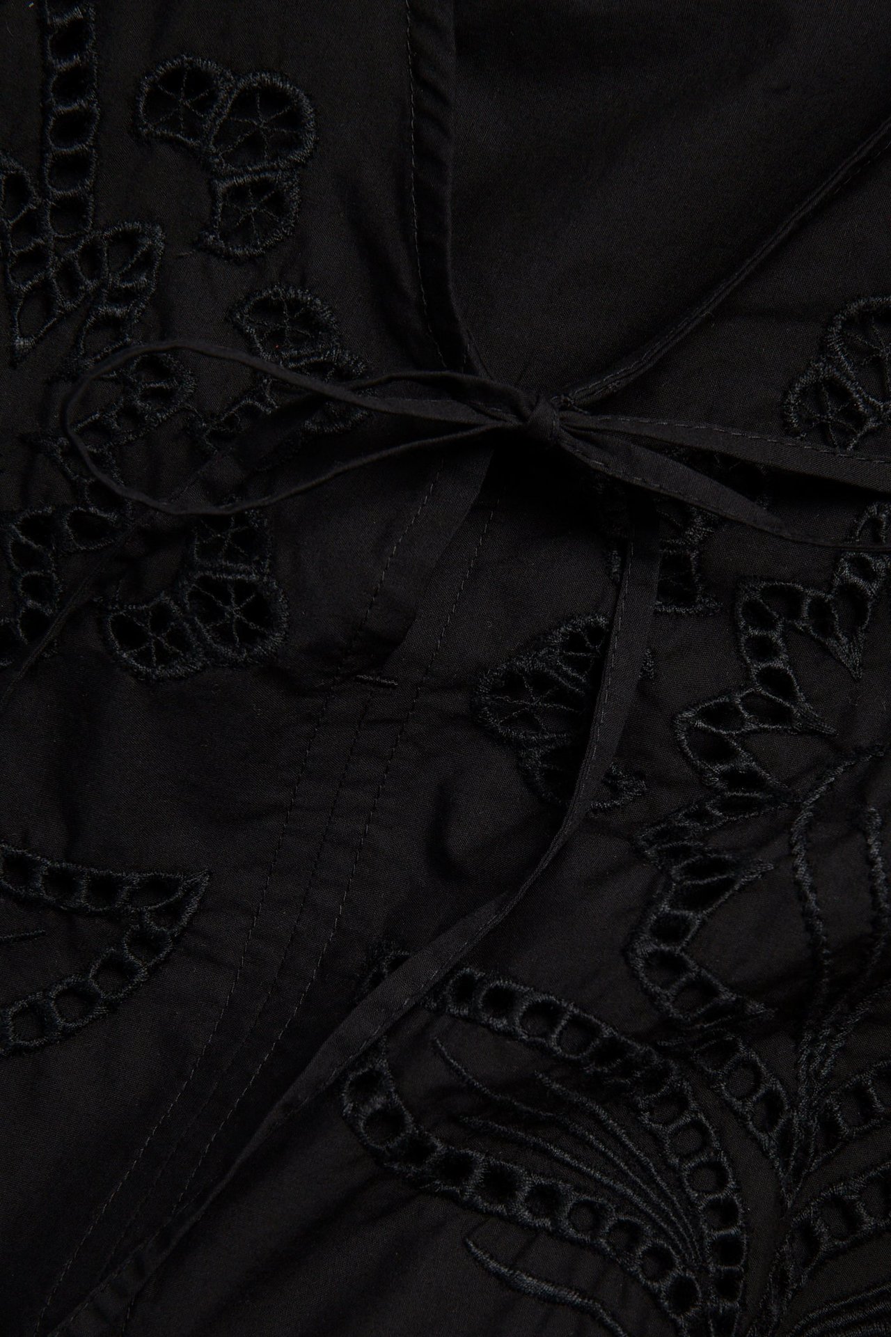 Lähikuva mustasta puuvillapopliinipuserosta, jossa brodeeraus ja sidottu vyötärö.