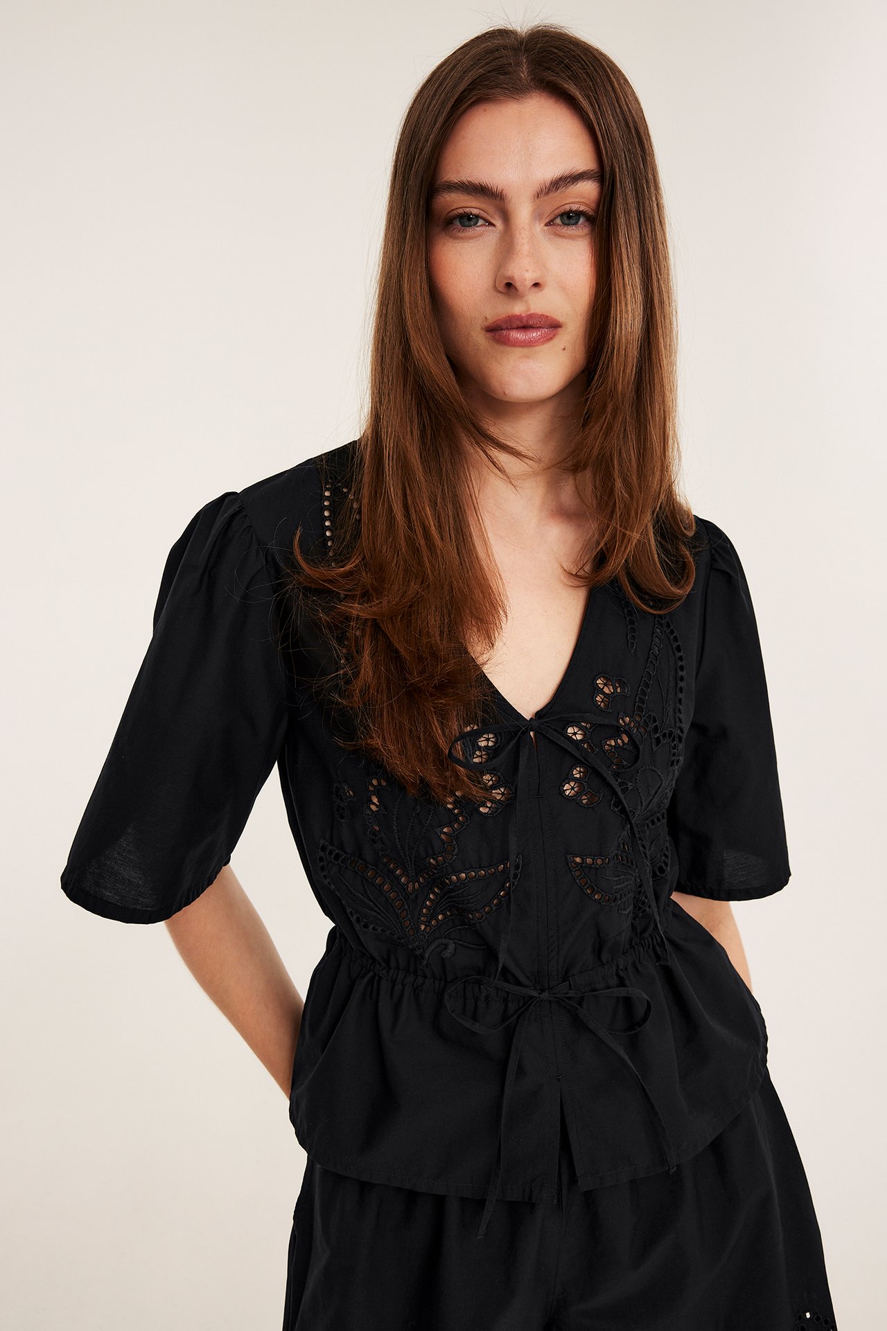 Widok z przodu kobiety w czarnej bluzce z popeliny bawełnianej z haftem, wiązaniem w pasie i pasującymi szortami.