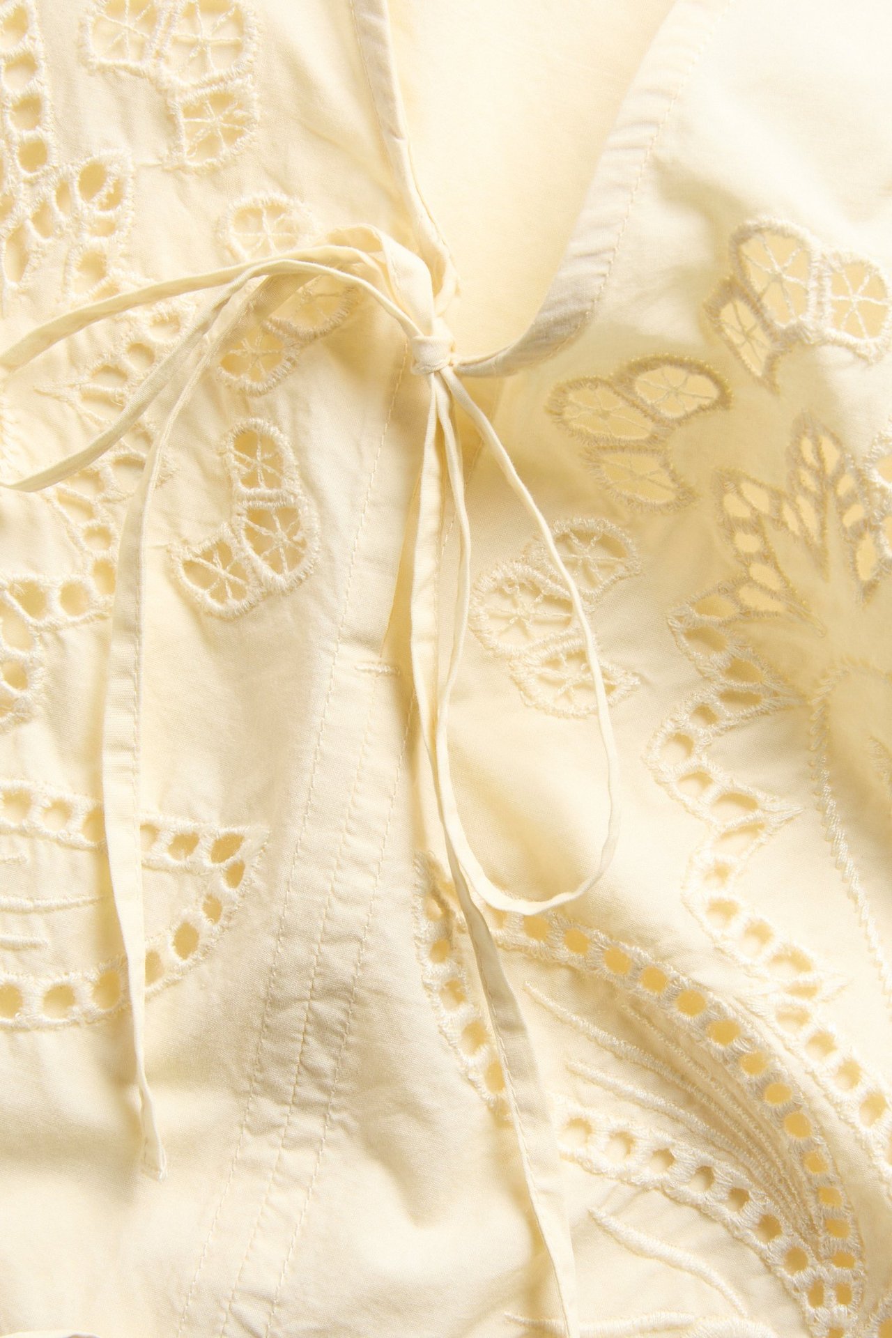 Zbliżenie na jasnożółtą bluzkę z popeliny bawełnianej z białym haftem i wiązaniem z przodu.