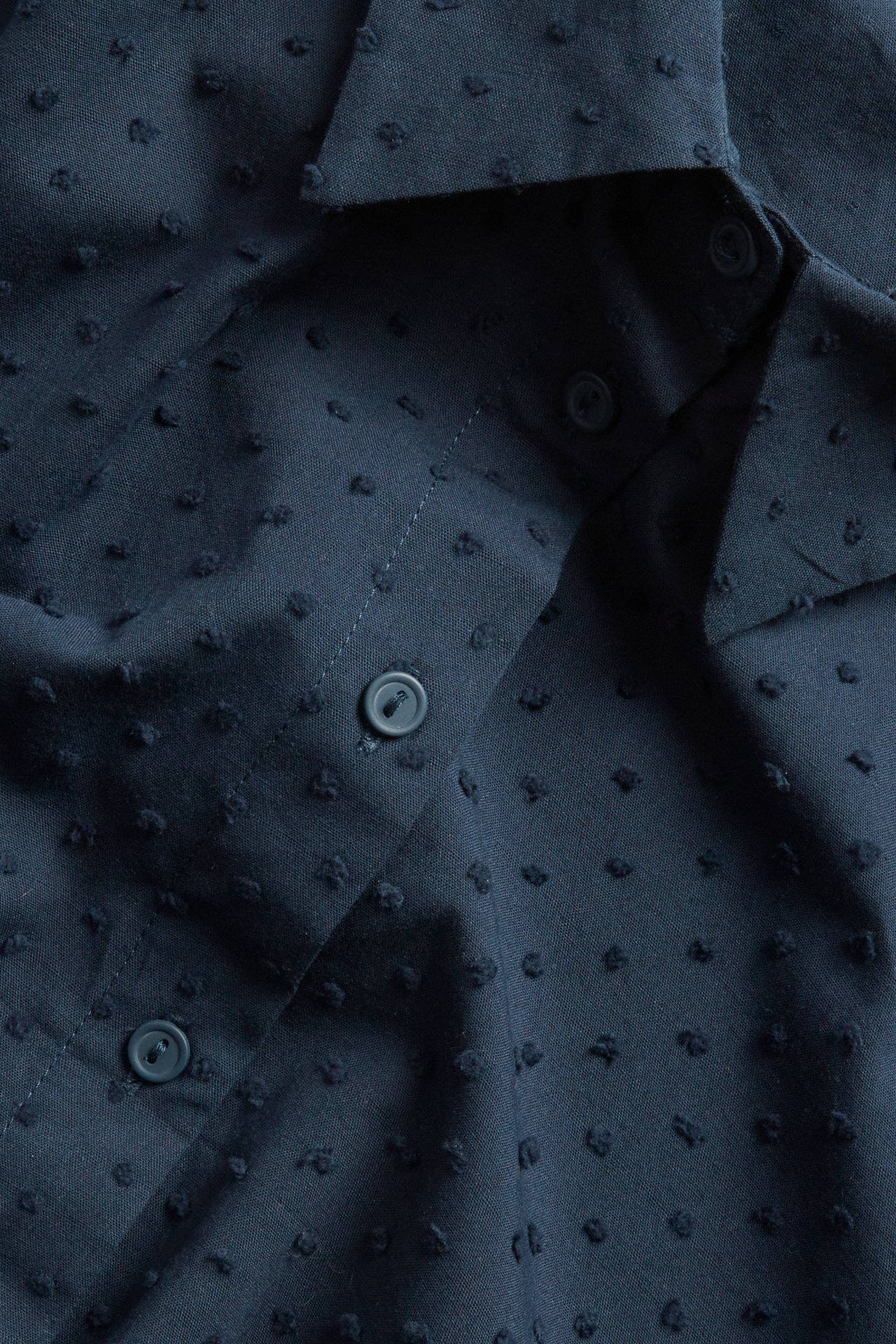 Närbild på en mörkblå kortärmad skjorta i bomull med prickigt mönster och synliga knappar.