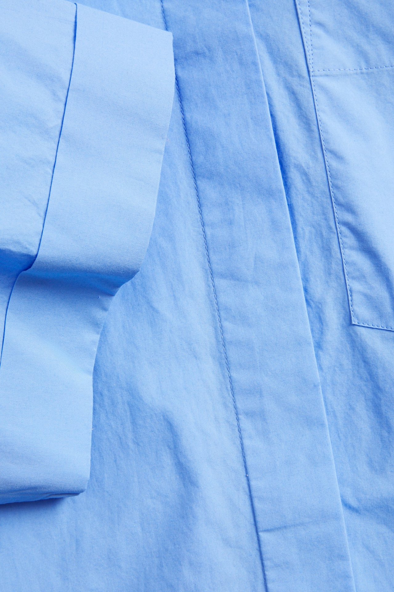 Nærbilde av en lyseblå kortermet skjorte i bomullspoplin med oppbrettet erme og brystlomme.