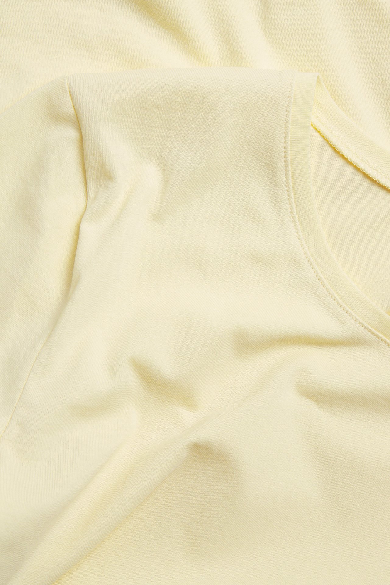Zbliżenie, widok z góry, na jasnożółty, jednolity, krótki top basic z okrągłym dekoltem.