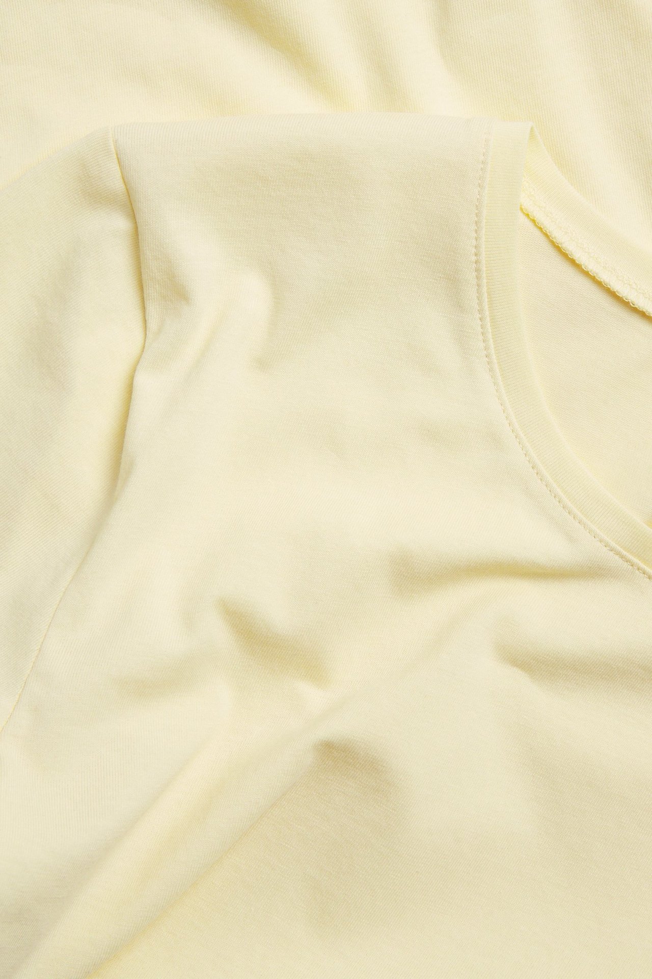 Zbliżenie, widok z góry, na jasnożółty, jednolity, krótki top basic z okrągłym dekoltem.