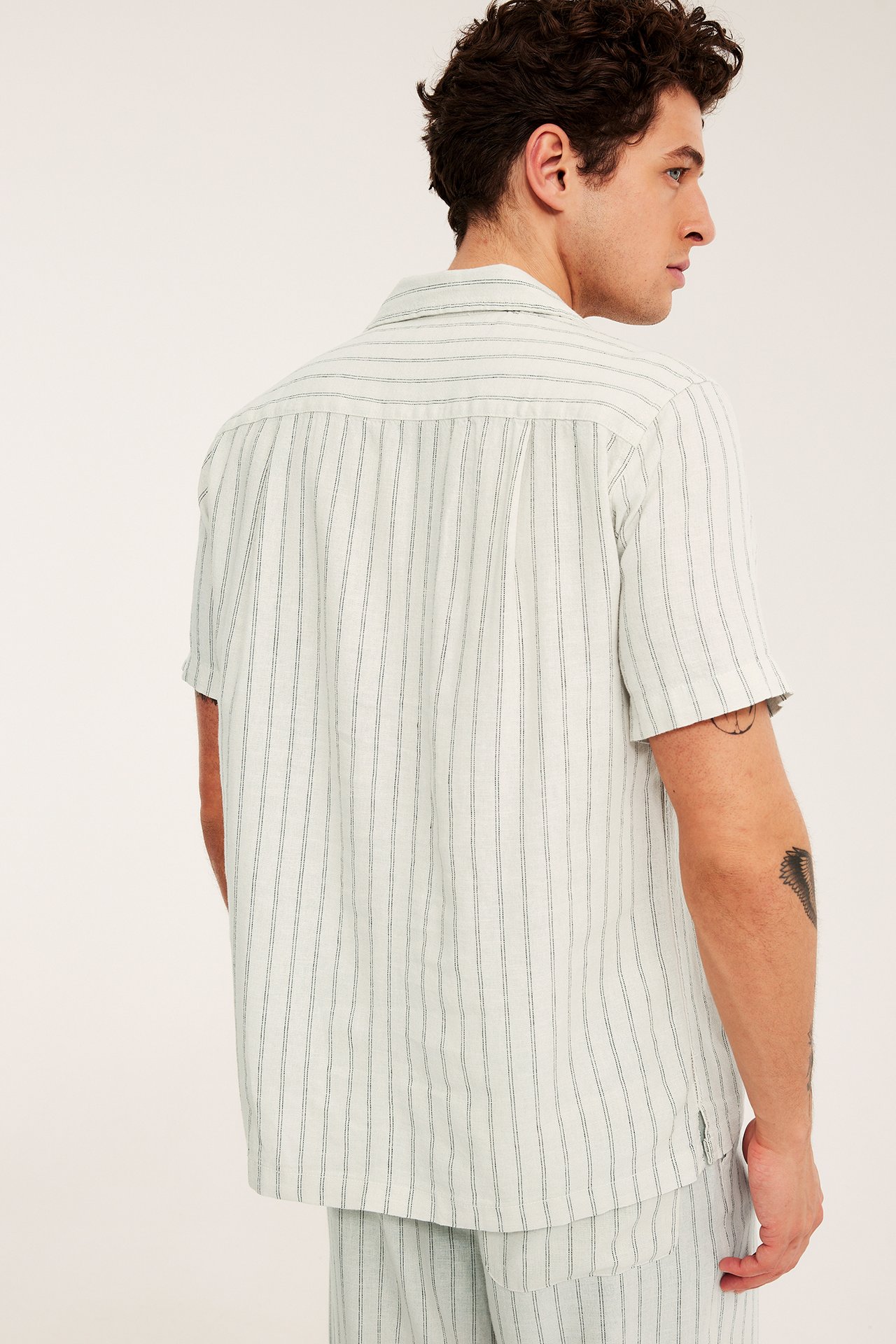 Widok z tyłu mężczyzny w jasnobeżowej, pasiastnej koszuli z krótkim rękawem z lnu i pasujących szortach.