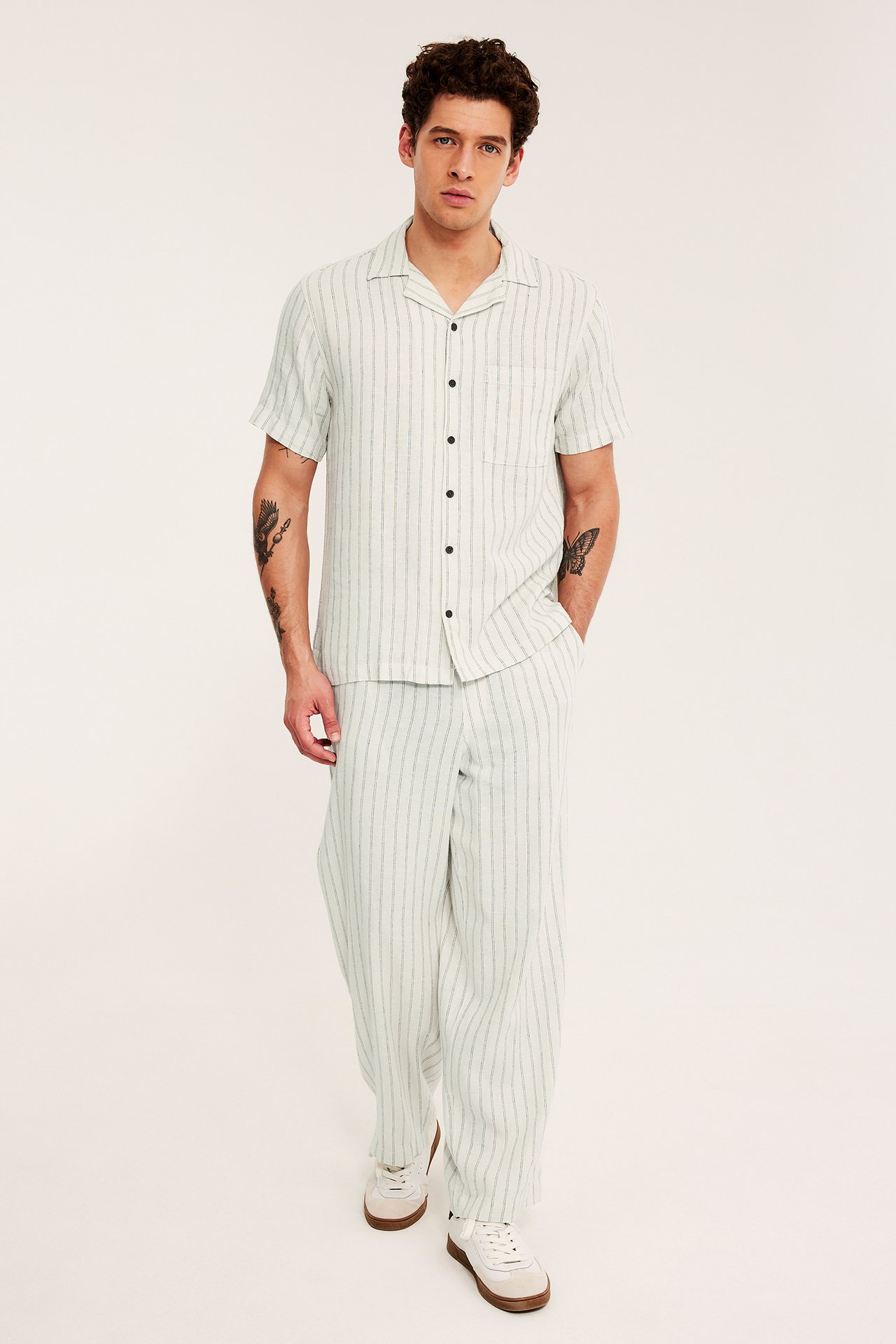 Frontbild av man i ljusbeige randig kortärmad resortsjorta, matchande byxor och vita sneakers.