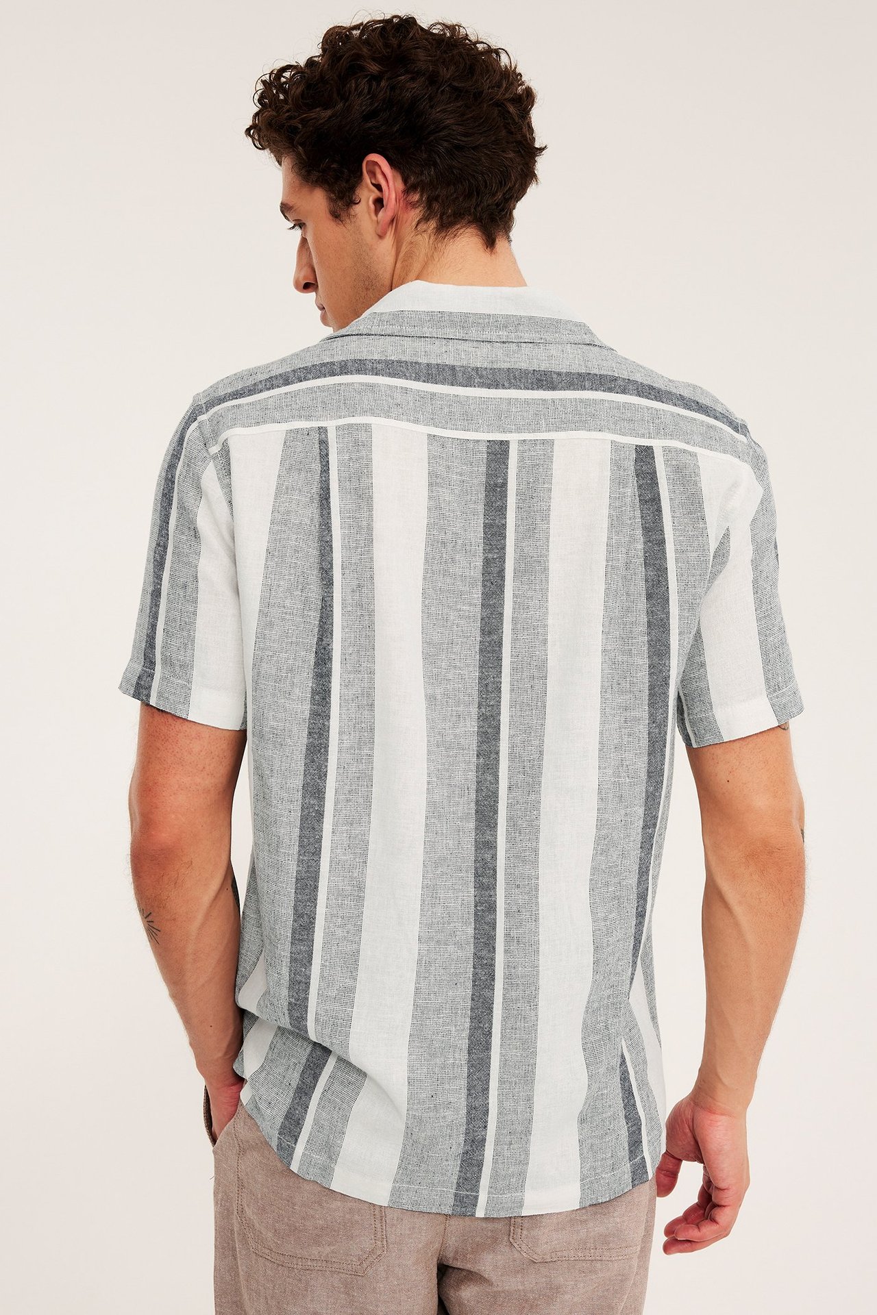 Mężczyzna od tyłu w paski granatowej i białej lniano-wiskozowej koszuli z krótkim rękawem.