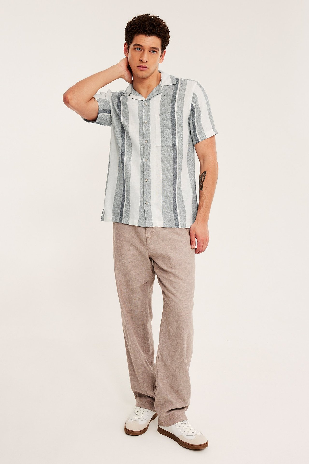 Frontvy: Mann i stripete mørkeblå og hvit kortermet resortskjorte, beige bukser og hvite joggesko.