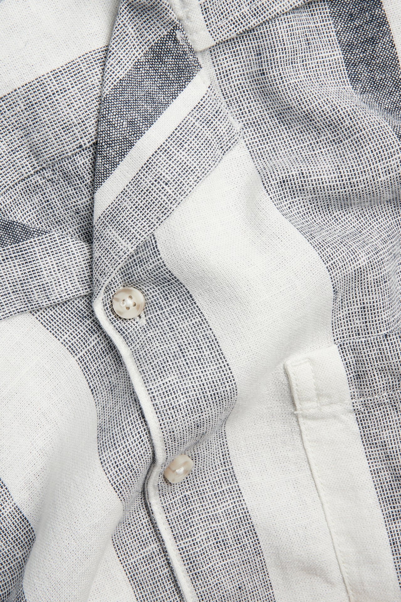 Nærbilde av en mørkblå og hvitstripet herreskjorte i lin/viskoseblanding med knapper og brystlomme.
