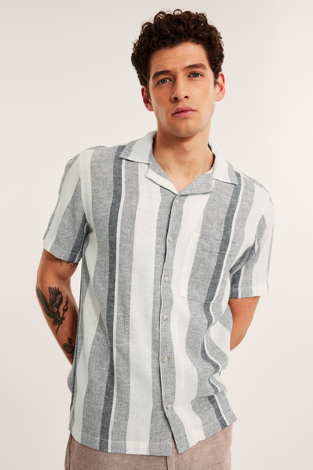 Framfra: mann i mørkeblå- og hvitstripet kortermet linblandings-resortskjorte med lysbrune bukser.