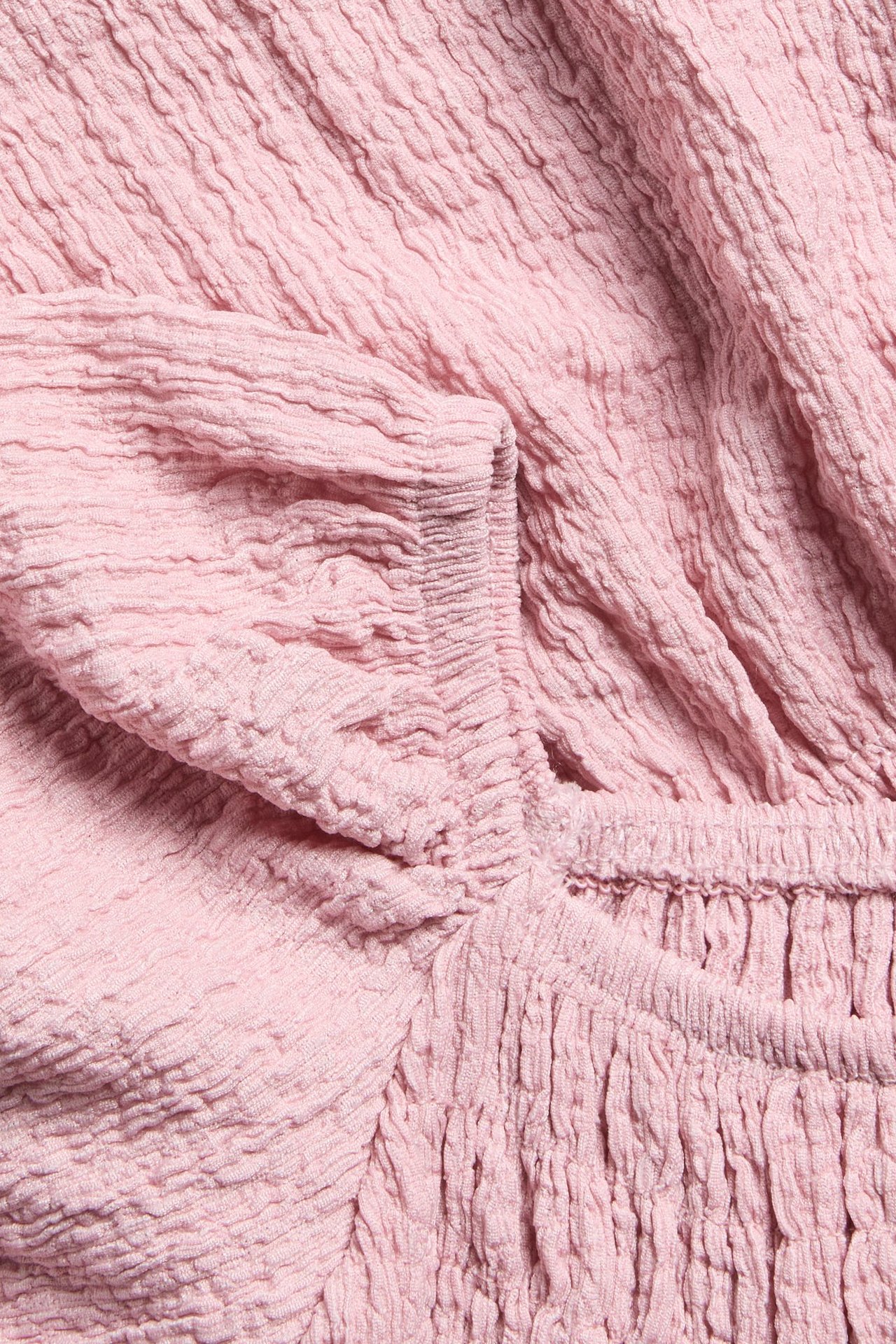 Närbild på en ljusrosa krinklad topp i trikå med smockdetaljer och resår i ärmslut.