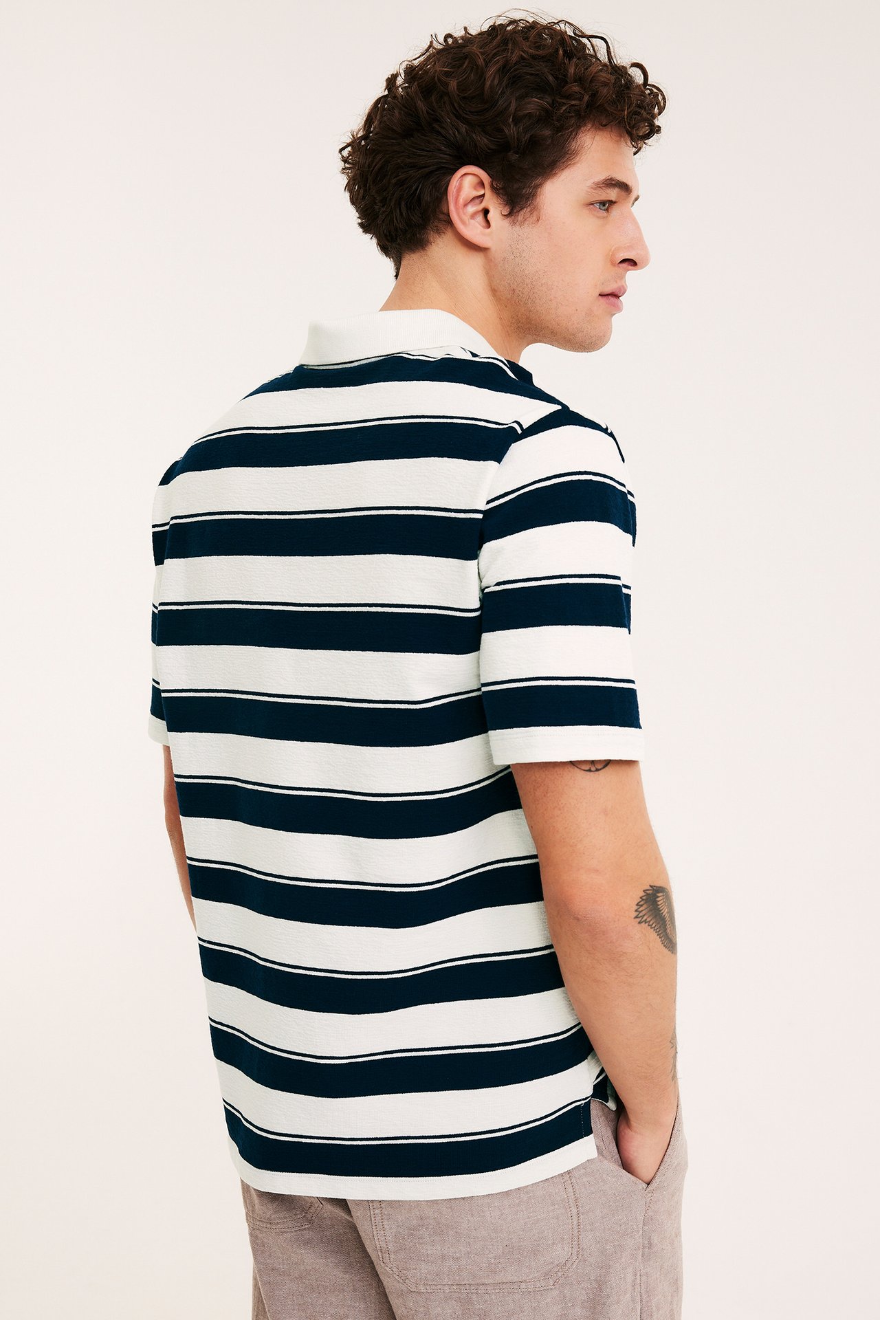 Mies sivukuvassa yllään raidallinen tummansinivalkoinen lyhythihainen pikeepaita ja beiget shortsit.