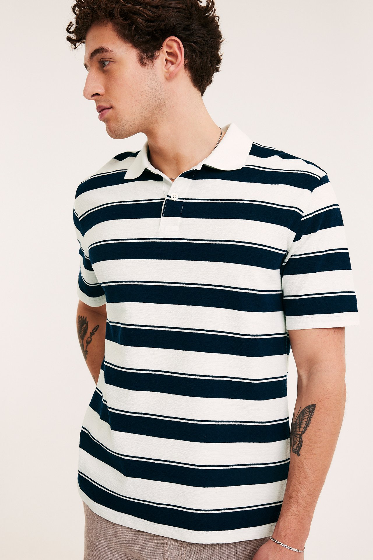 Mies yllään tummansinivalkoraidallinen lyhythihainen puuvillapoolopaita, jossa on kaksi nappia, sivukuva.