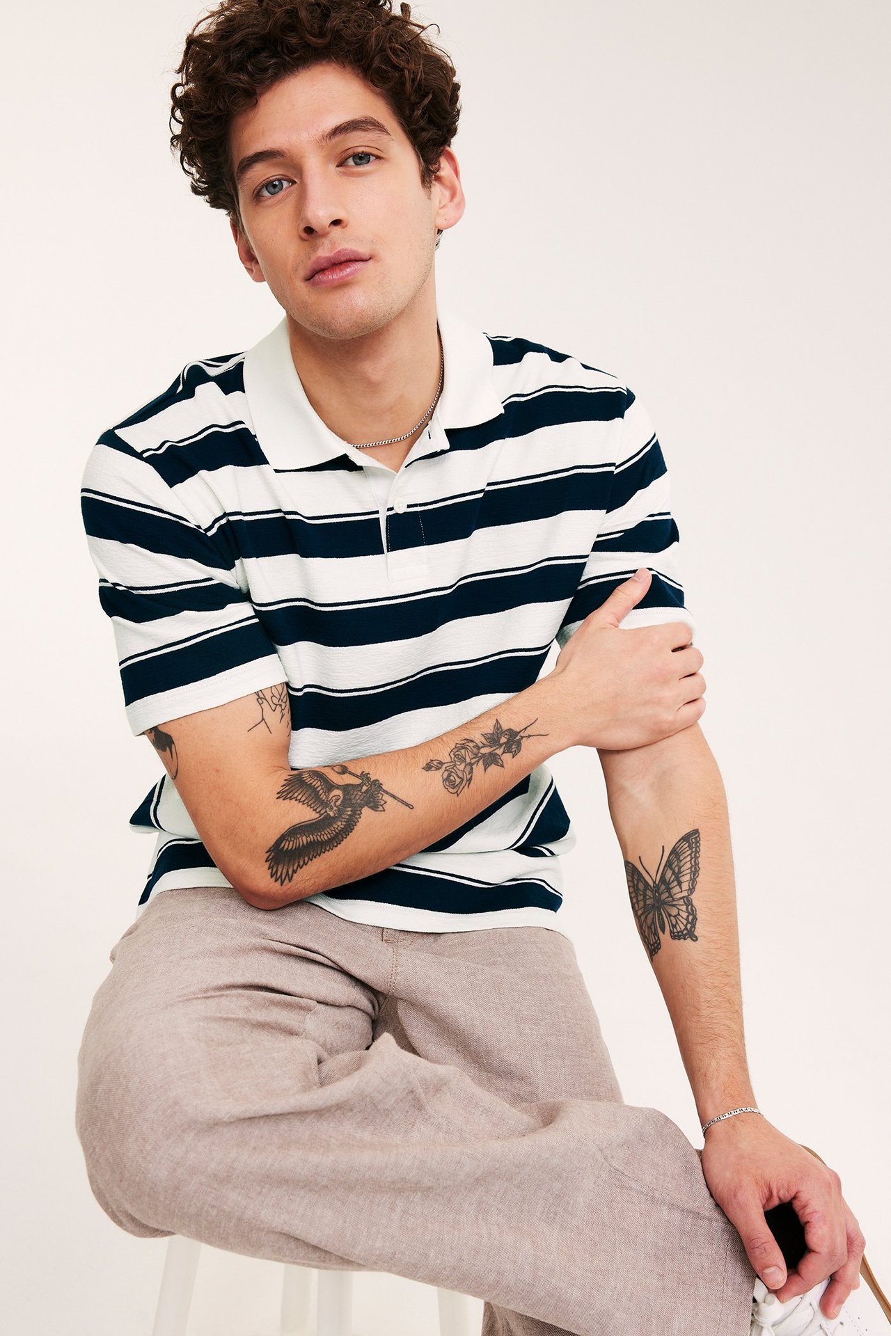 Edestäpäin, mies tummansinisessä ja valkoisessa raidallisessa pikeepaidassa, valkoinen kaulus ja beiget housut.