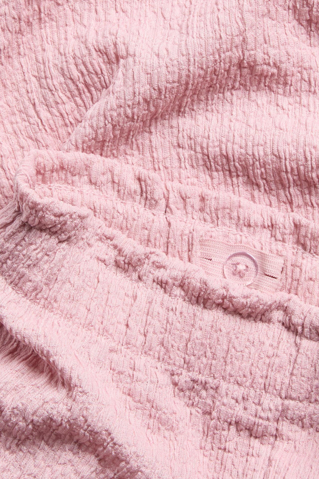 Zbliżenie na jasnoróżowe marszczone spodnie culotte z elastyczną talią i wewnętrznym guzikiem.