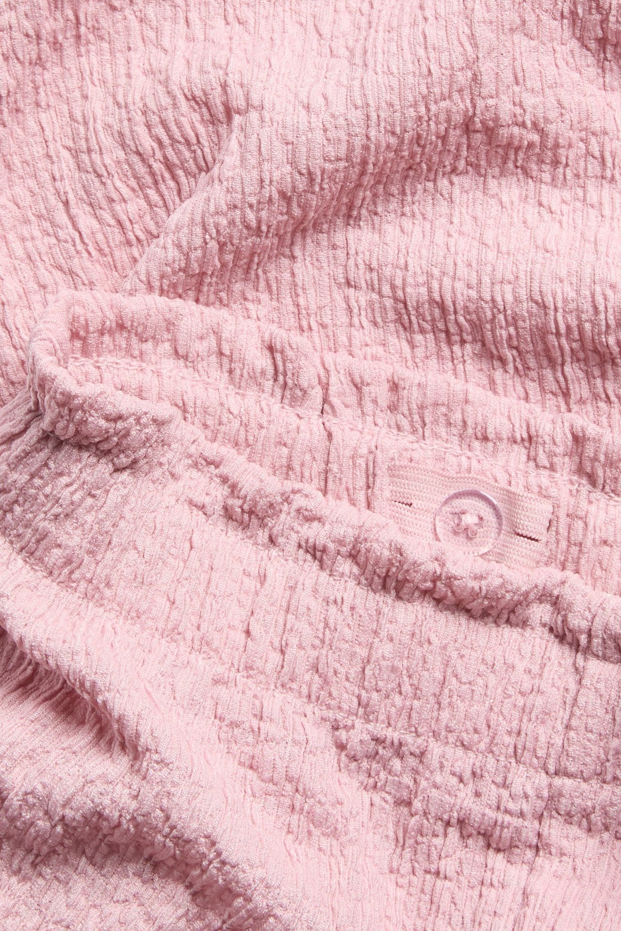 Zbliżenie na jasnoróżowe marszczone spodnie culotte z elastyczną talią i wewnętrznym guzikiem.