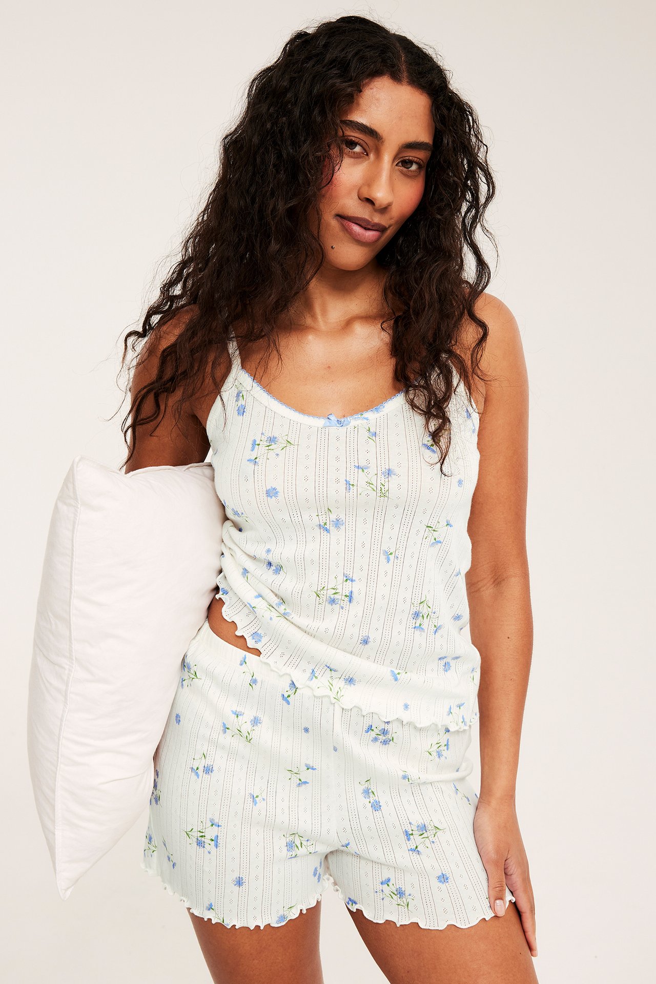 Frontbilde av en kvinne i lysblått blomstret pointelle pyjamasett, holder en hvit pute.