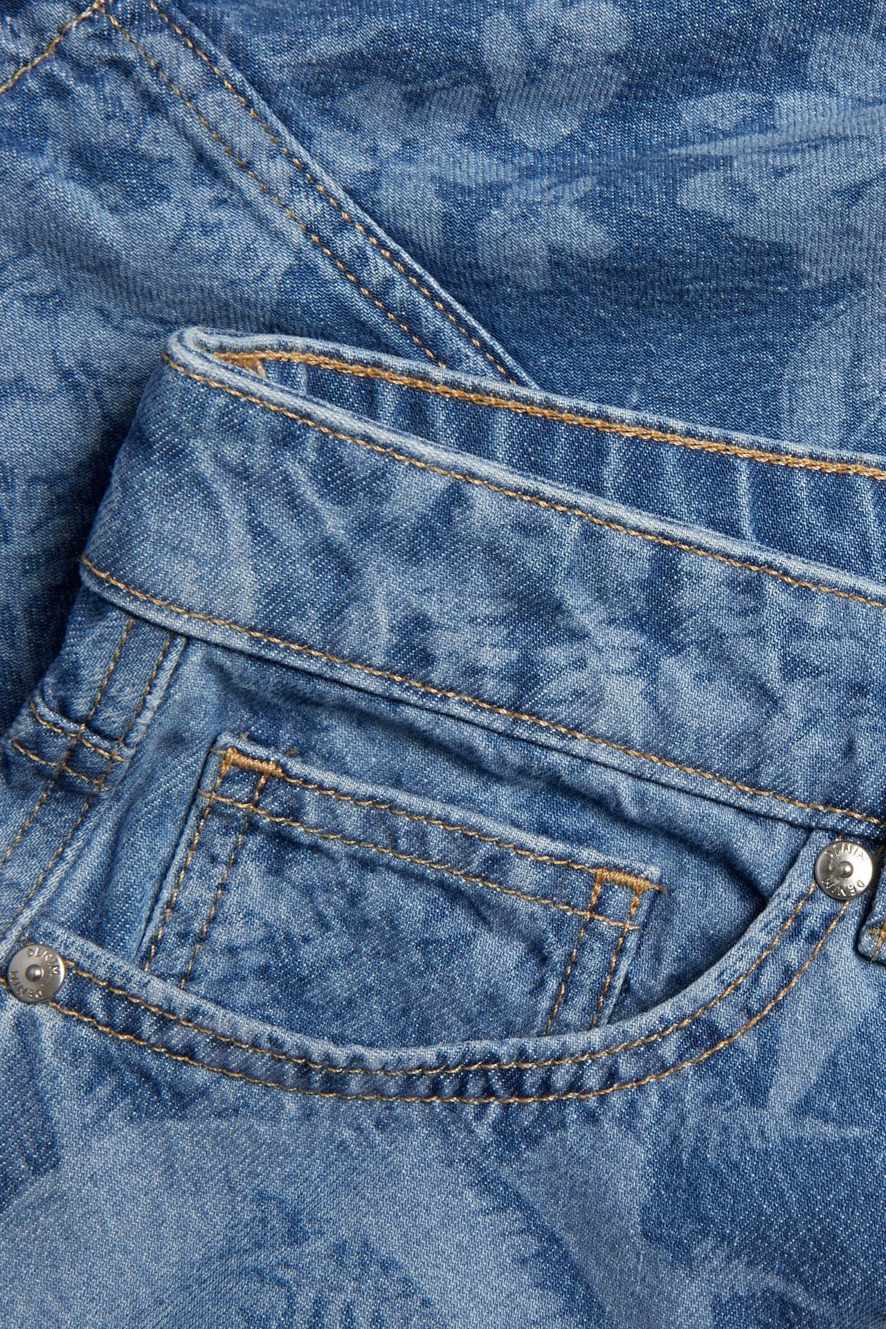 Zbliżenie na jasnoniebieską jeansową spódnicę w kwiaty, z widocznymi szwami, kieszenią i metalowym guzikiem.