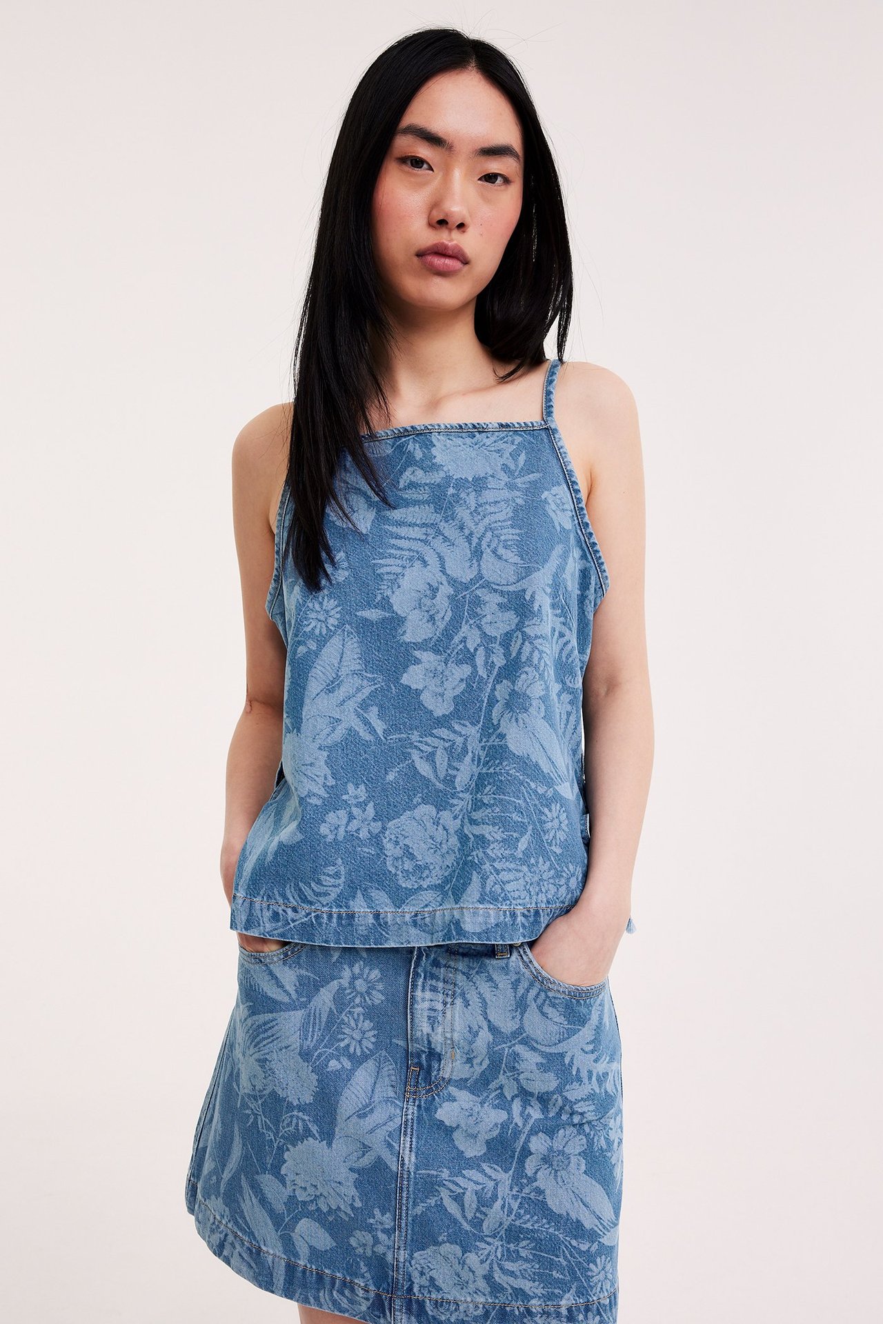 Edestäpäin nainen lyhyessä vaaleansinisessä kukallisessa farkkuhameessa ja yhteensopivassa camisole-topissa.