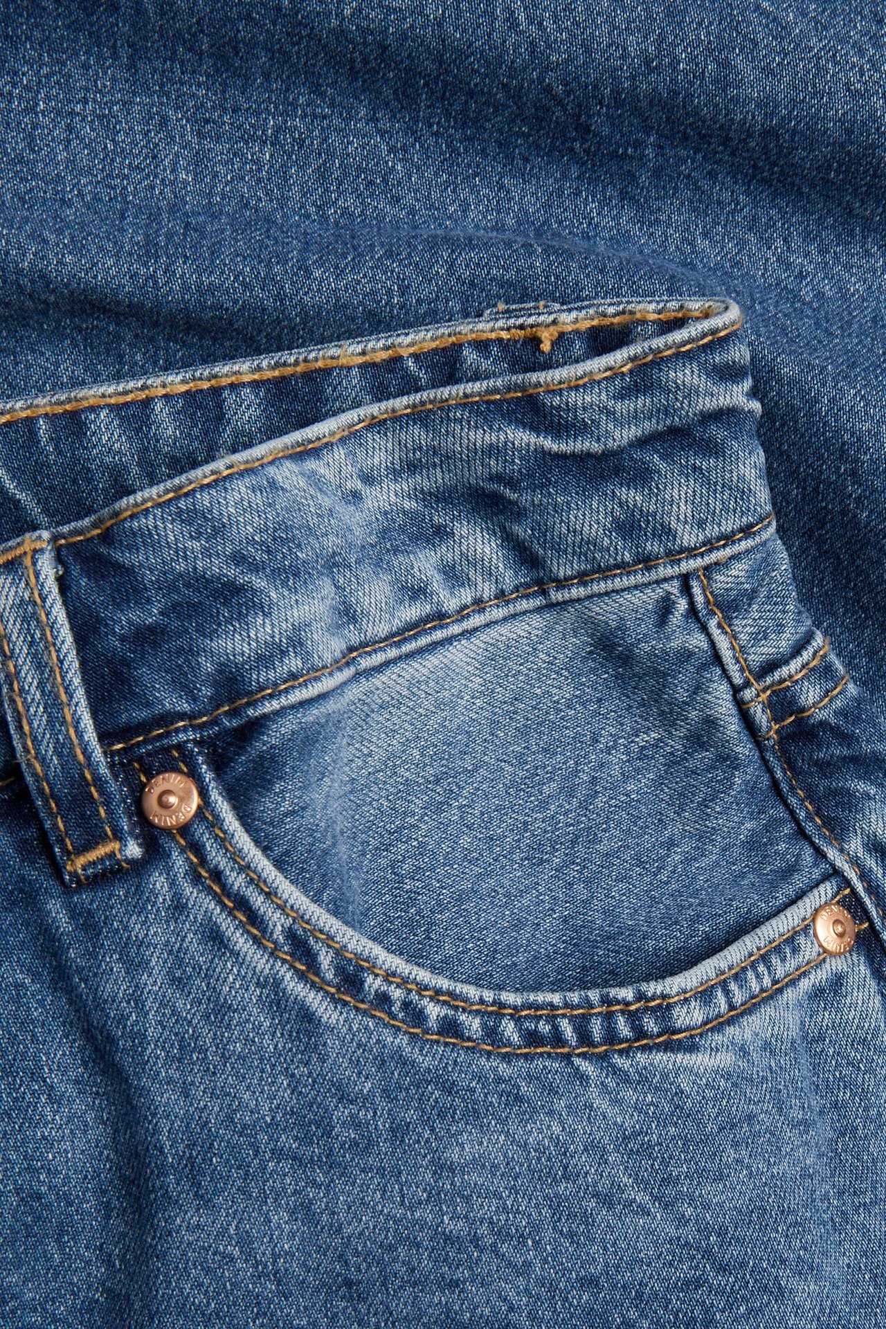 Lähikuva sinisistä denimshortseista, jossa näkyy etutasku, tikkaukset ja metalliniitit.