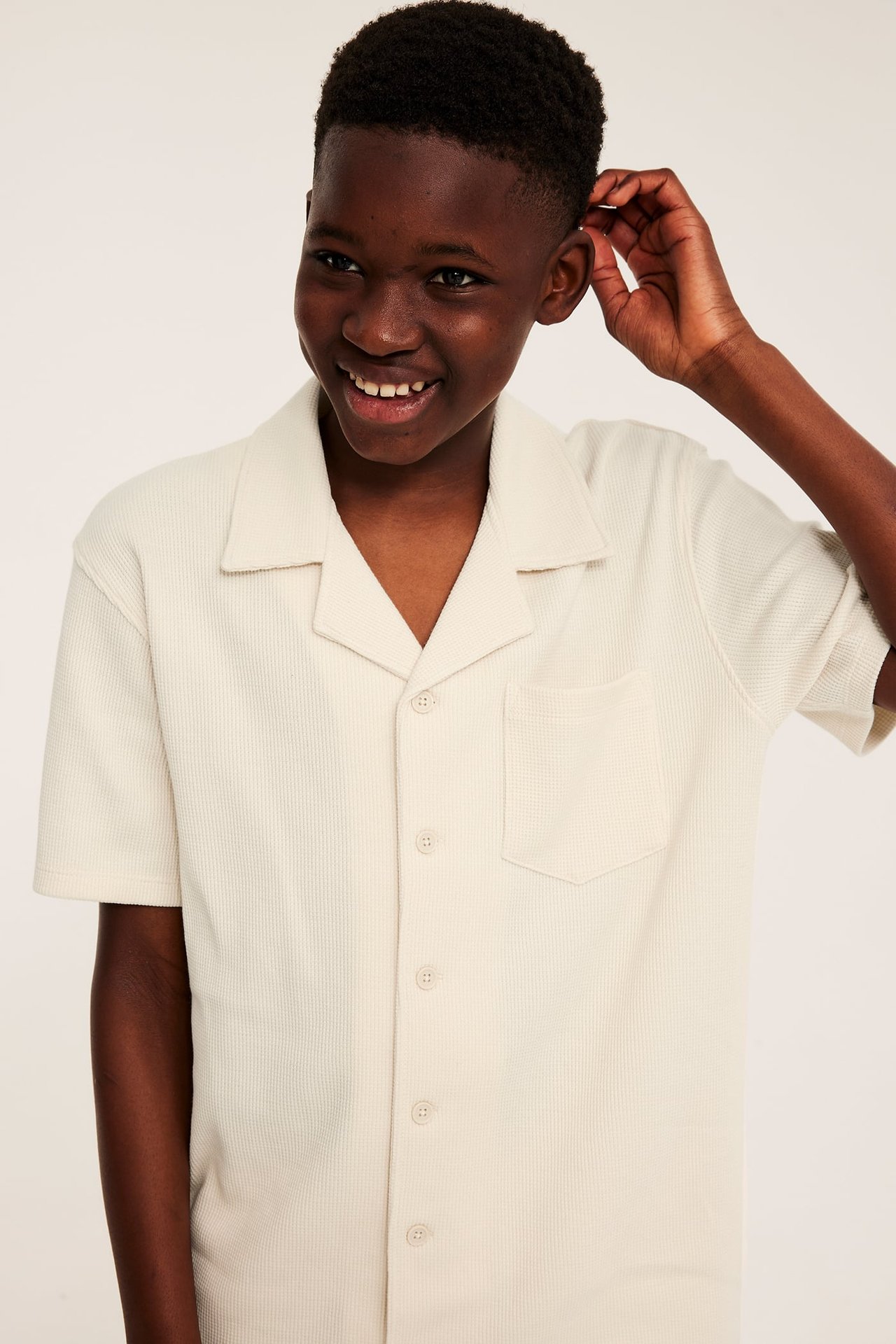 Framsida av leende barn i ljusbeige våfflad bomullsskjorta med kort ärm och resortkrage.