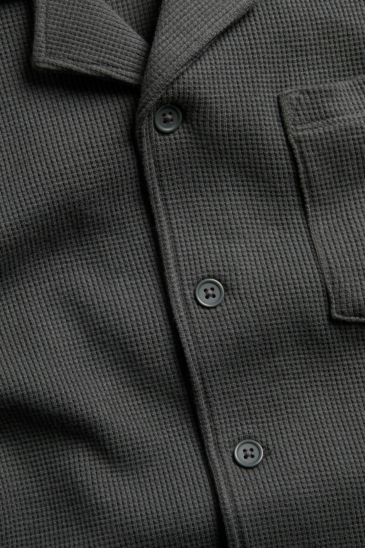 Zbliżenie, widok z przodu, czarnej bawełnianej koszuli w waflowej strukturze z kołnierzykiem resortowym i guzikami.