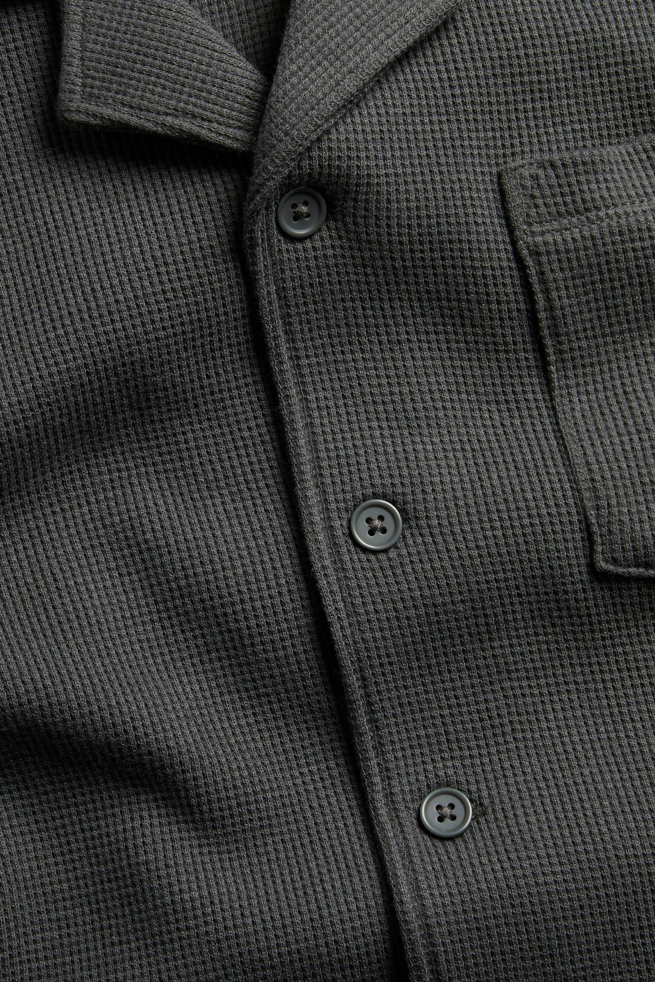 Zbliżenie, widok z przodu, czarnej bawełnianej koszuli w waflowej strukturze z kołnierzykiem resortowym i guzikami.