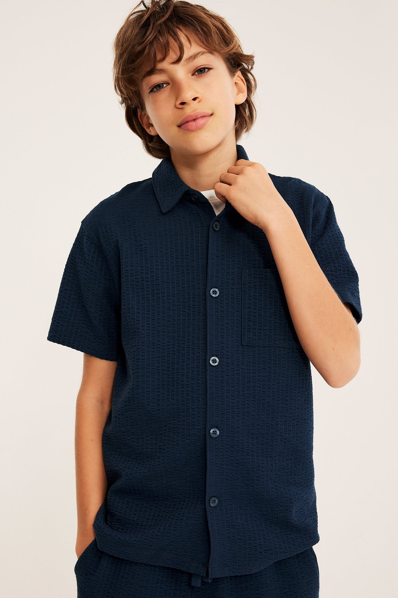 Widok z przodu: chłopiec w granatowej koszuli seersucker z krótkim rękawem na białym podkoszulku.