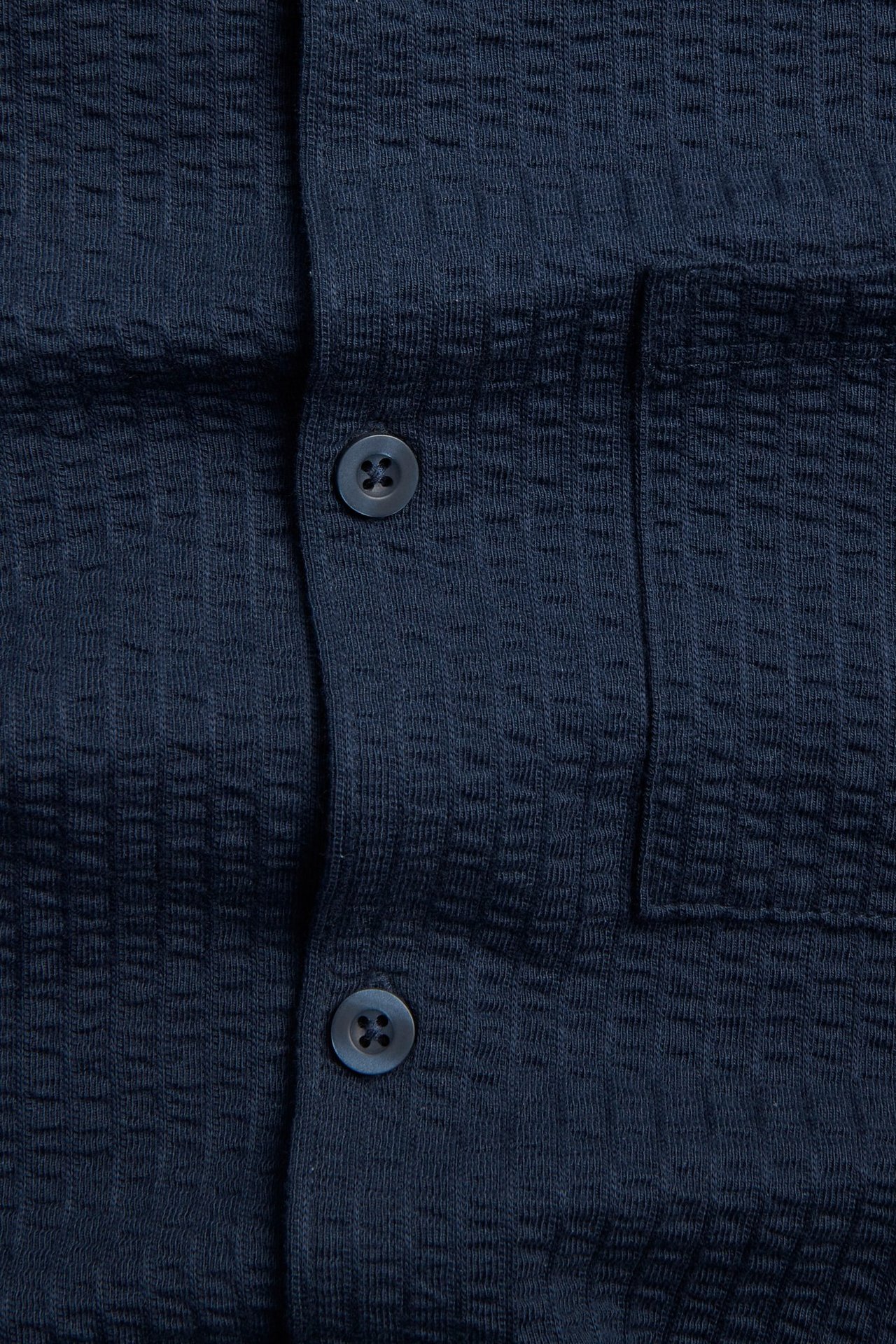 Zbliżenie ciemnoniebieskiej bawełnianej koszuli seersucker z listwą guzikową i kieszenią na piersi.