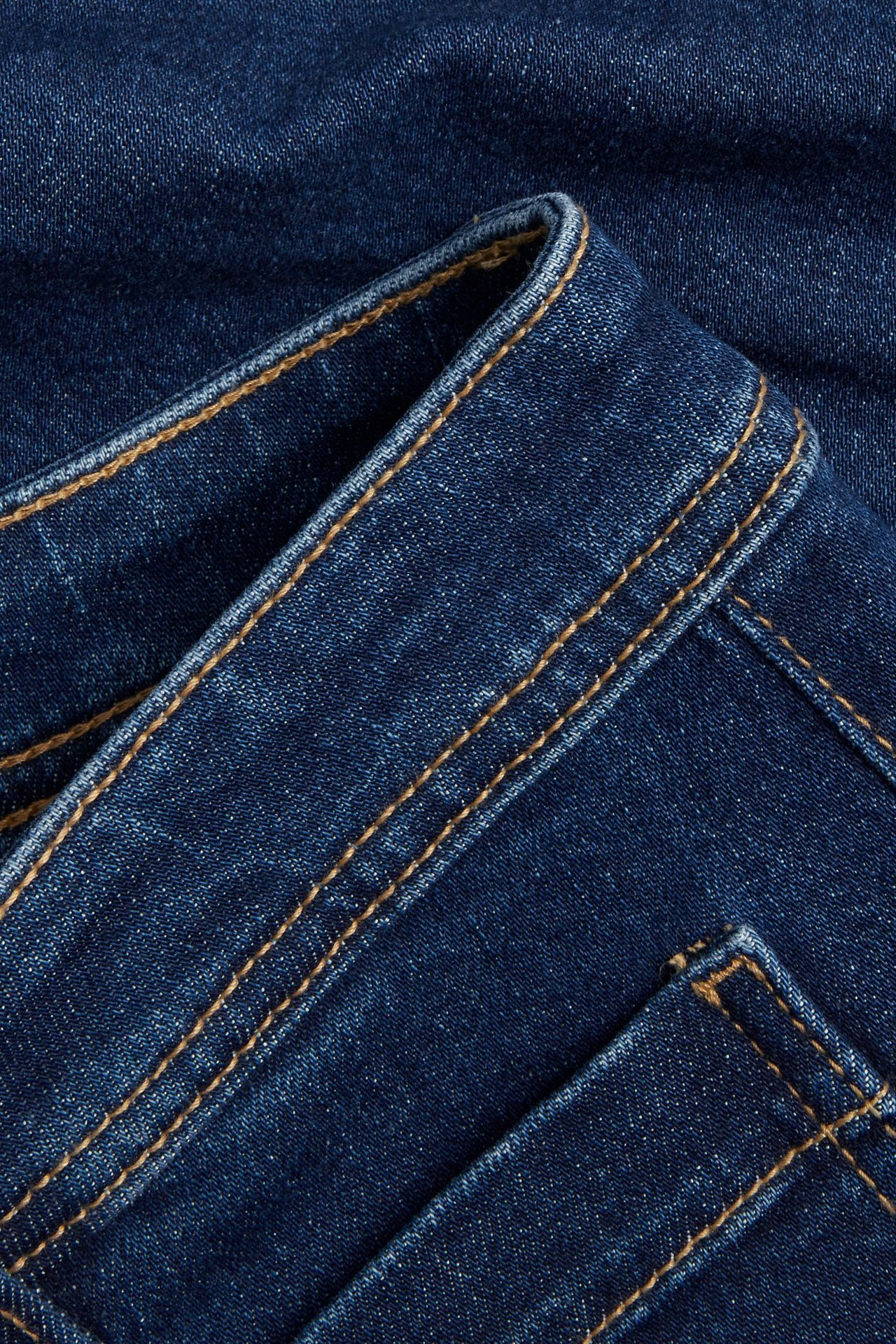 Nærbilde av mørkeblå denimshorts med oransje sømmer, viser linning og lommedetalj.