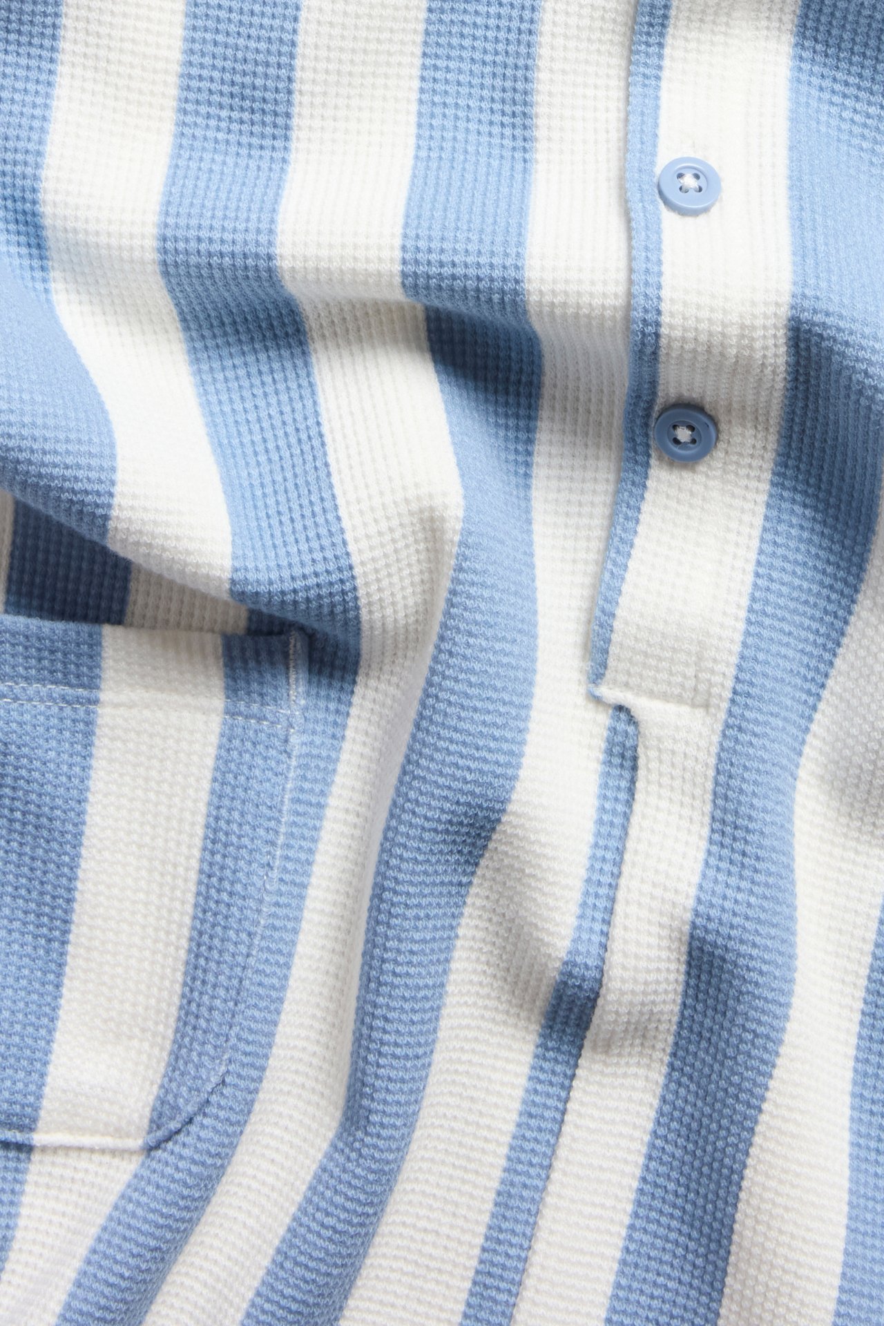 Lähikuva vauvan raidallisesta vaaleansinisestä ja valkoisesta vohvelipuvusta, jossa napit edessä ja tasku.