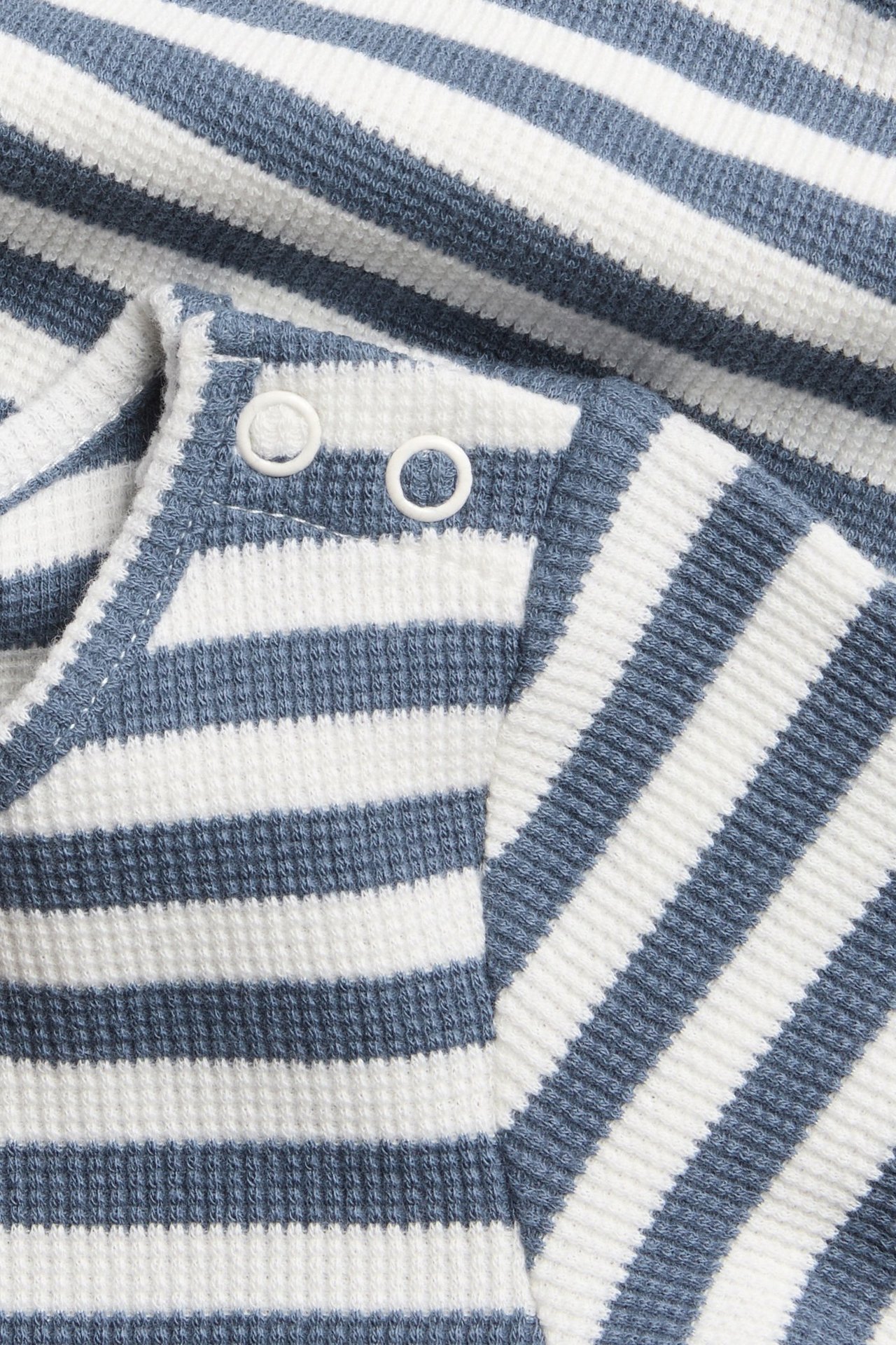 Lähikuva vauvan sinivalkoraidallisesta vohvelikankaasta tehdystä body-paidasta, valkoiset painonapit olkapäässä.