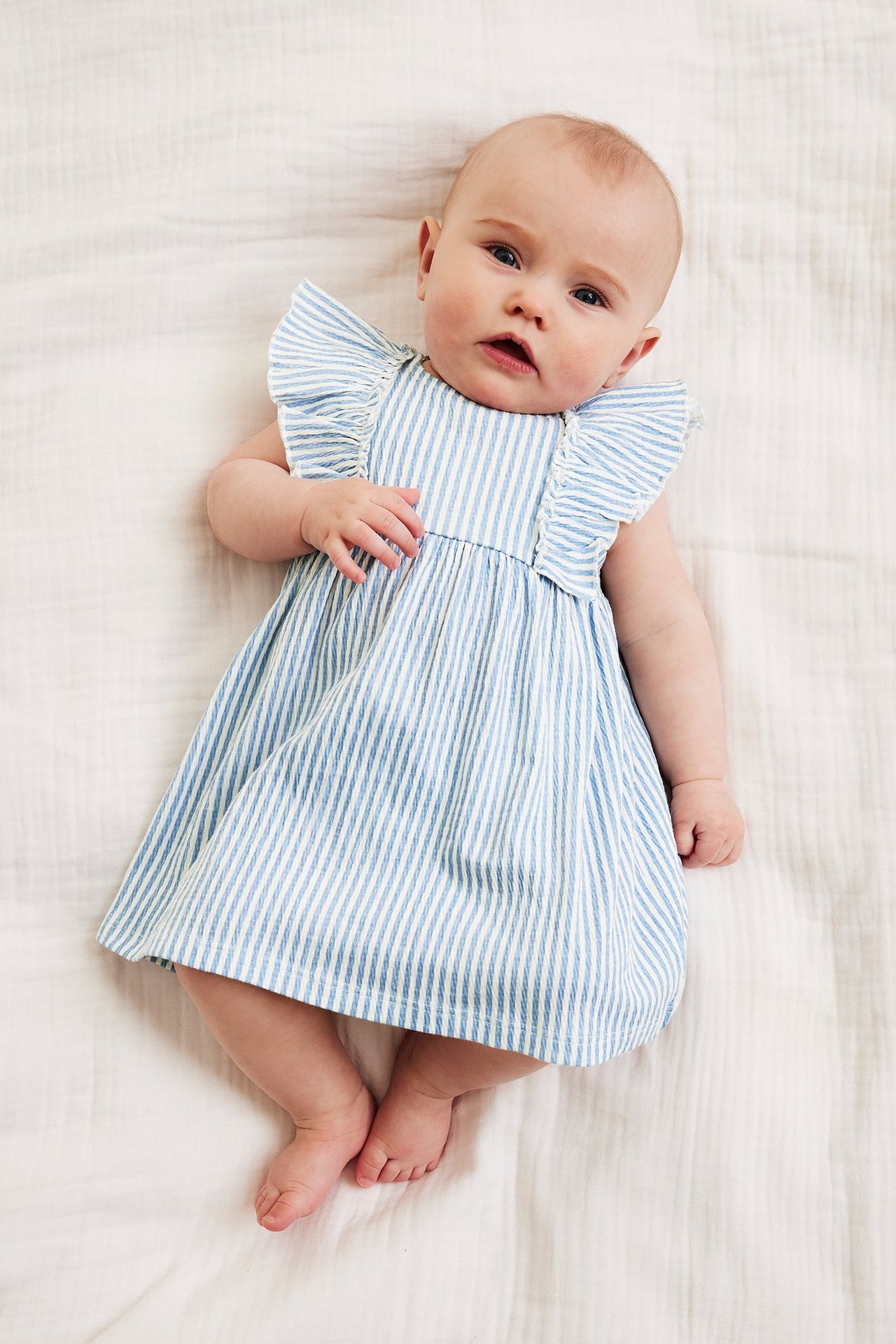 Widok z góry na niemowlę w jasnoniebiesko-białej sukience w paski z falbanami.