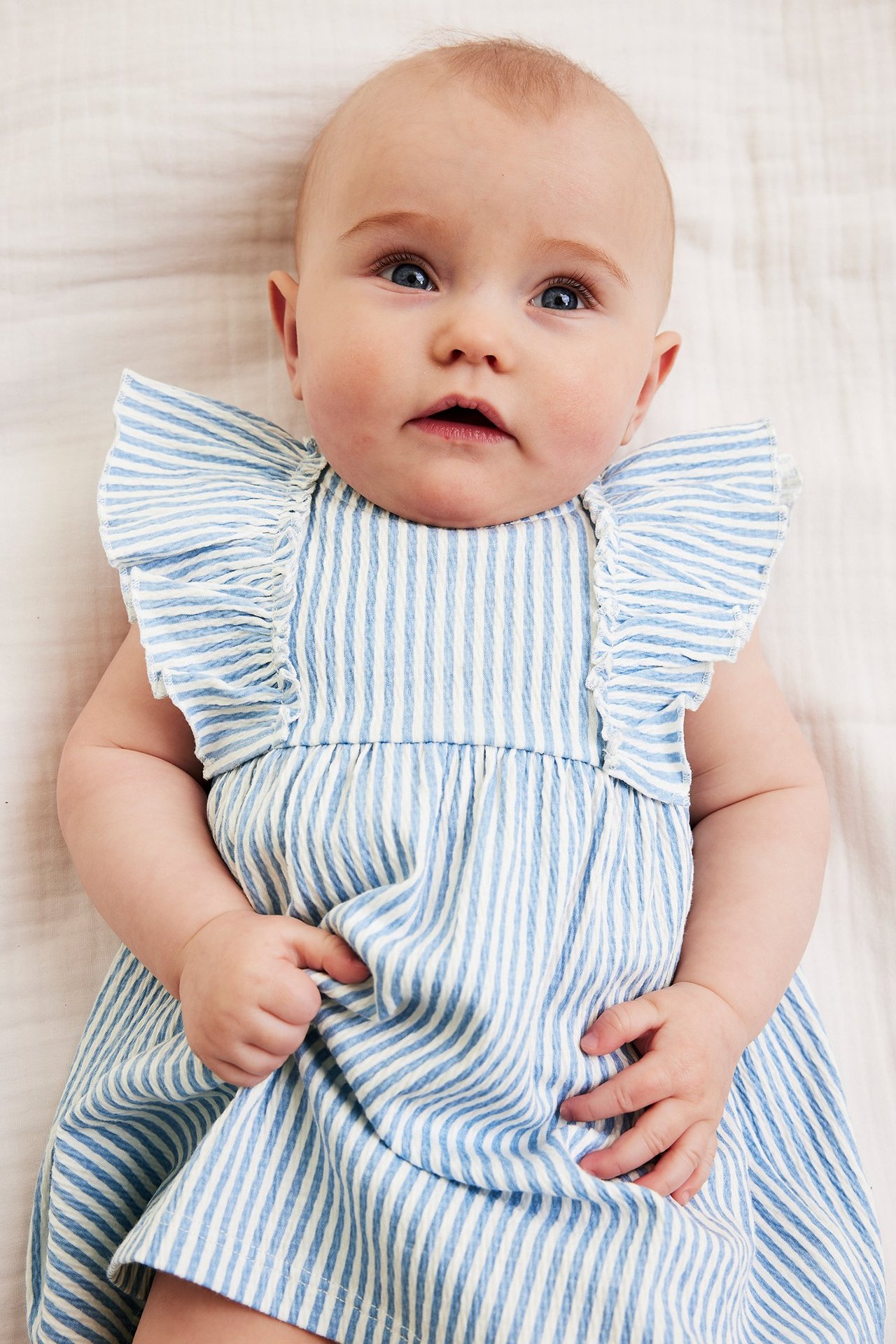 Vauva edestä: vaaleansinivalkoraidallinen kreppijersey-mekko röyhelöhihoilla.