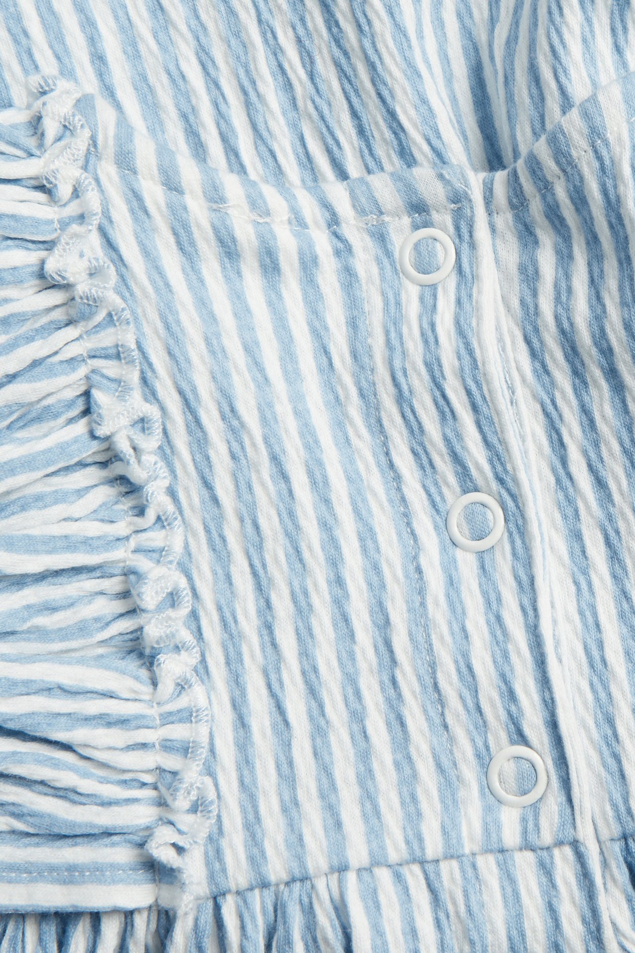 Lähikuva vaaleansinisestä ja valkoisesta raidallisesta crepe-vauvanmekosta, jossa röyhelöitä ja nepparit.