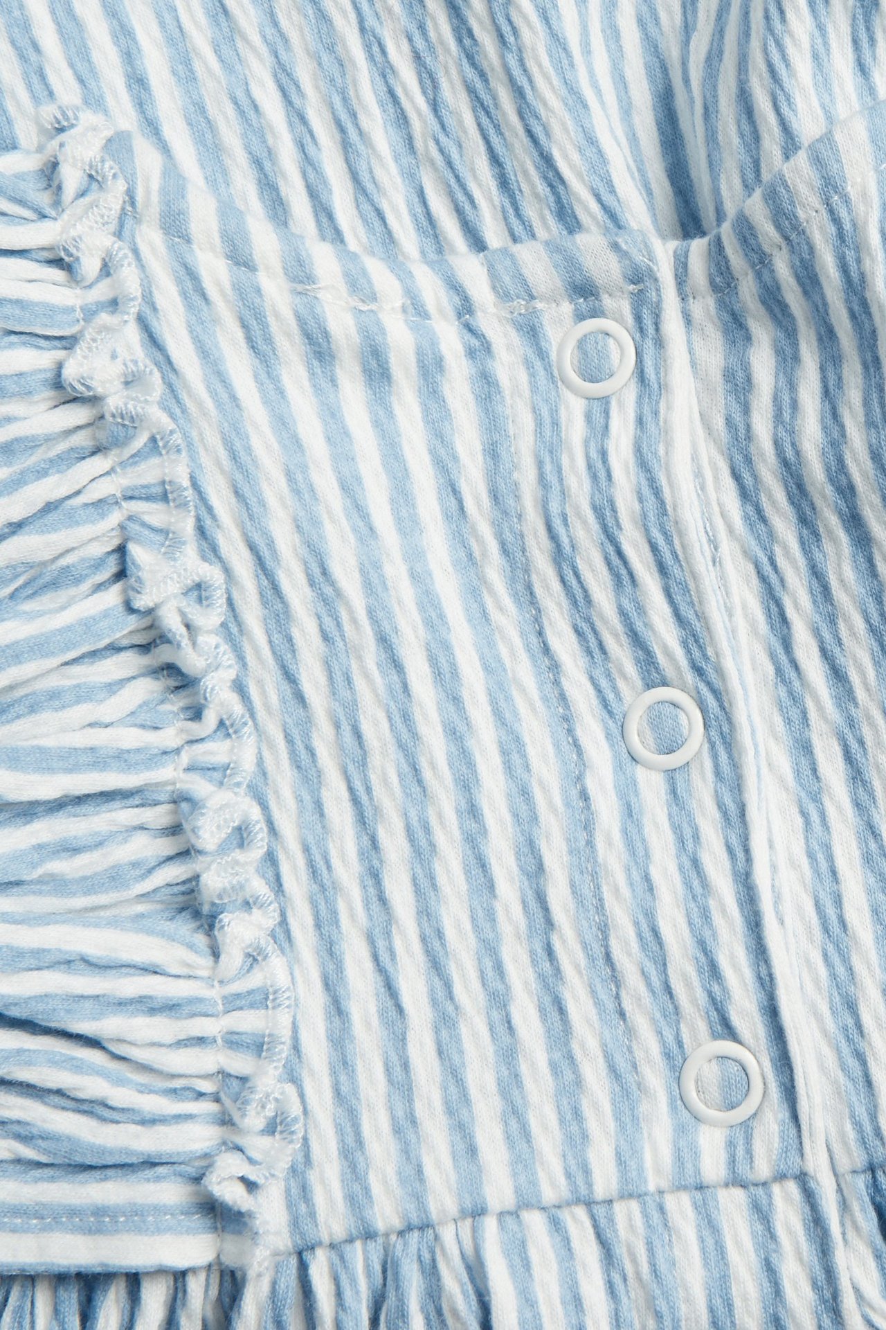 Zbliżenie na błękitno-białą sukienkę niemowlęcą w paski z krepy, z falbanami i zatrzaskami.